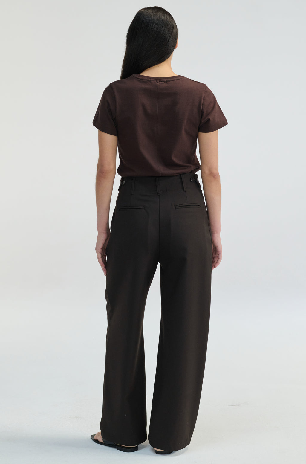 Woman wearing a brown t-shirt with dark brown trousers on a plain background
