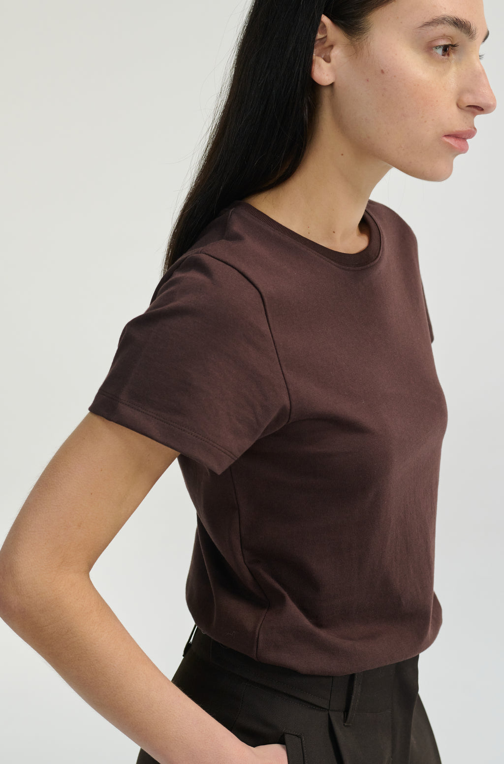 Woman wearing a brown t-shirt with dark brown trousers on a plain background