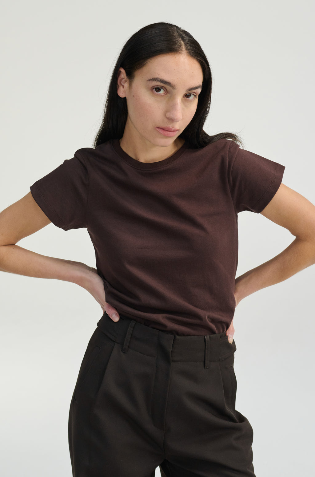 Woman wearing a brown t-shirt with dark brown trousers on a plain background