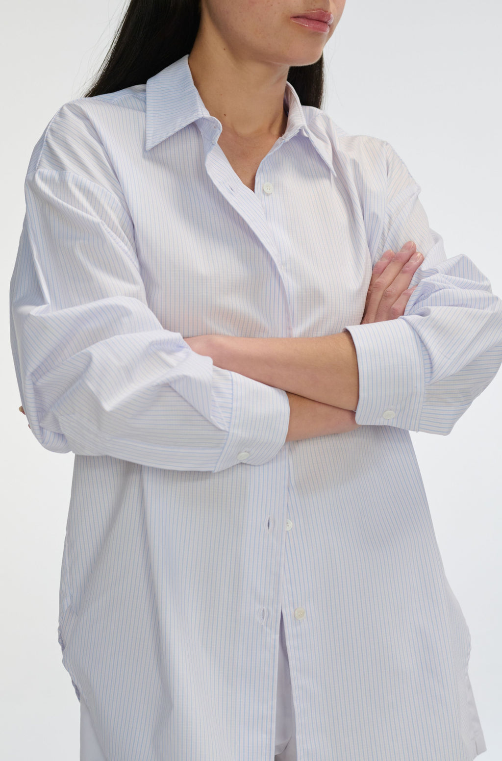 Woman wearing a light blue and white striped shirt with rolled-up sleeves on a white background