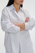 Woman wearing a light blue and white striped shirt with rolled-up sleeves on a white background