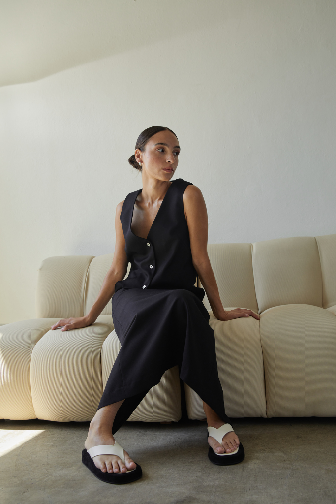 Woman in a black sleeveless top and pants sitting on a beige couch.