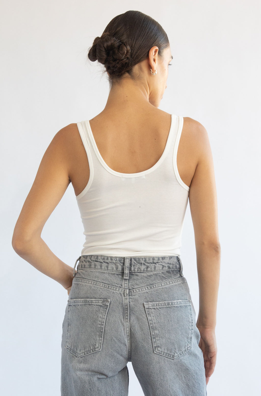 Person wearing a white tank top and light blue jeans against a plain background