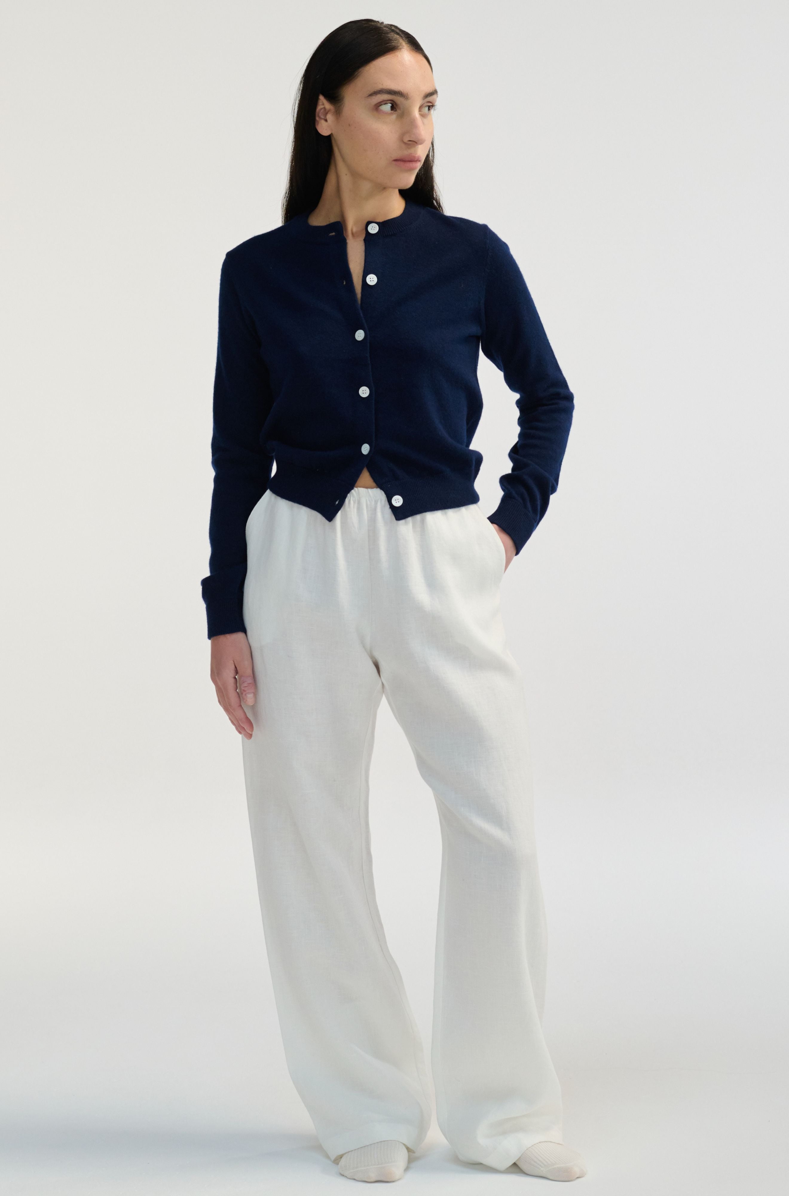 Woman wearing a navy cardigan and white pants on a white background