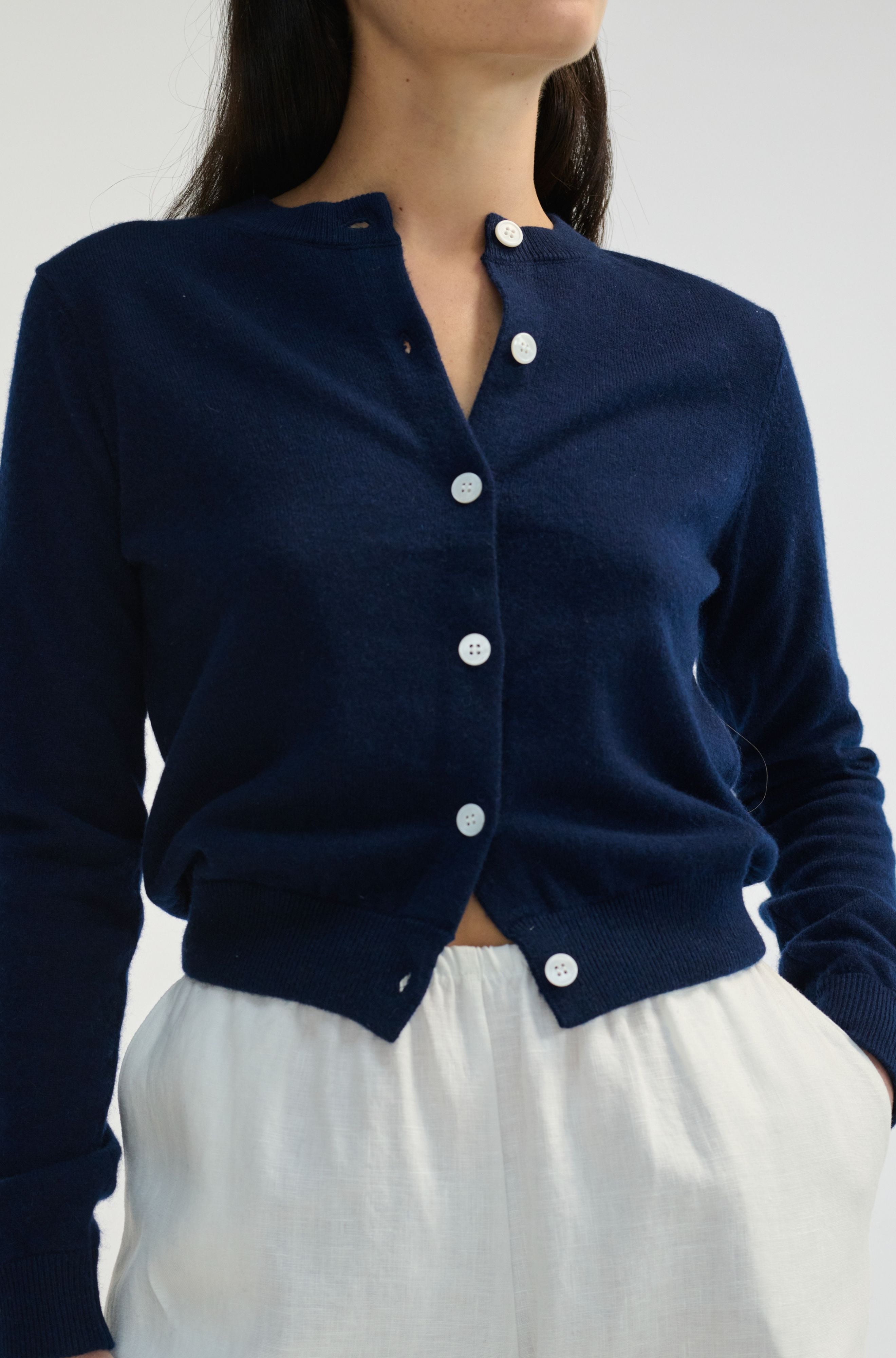 Navy blue cardigan with white buttons worn by a person on a plain background