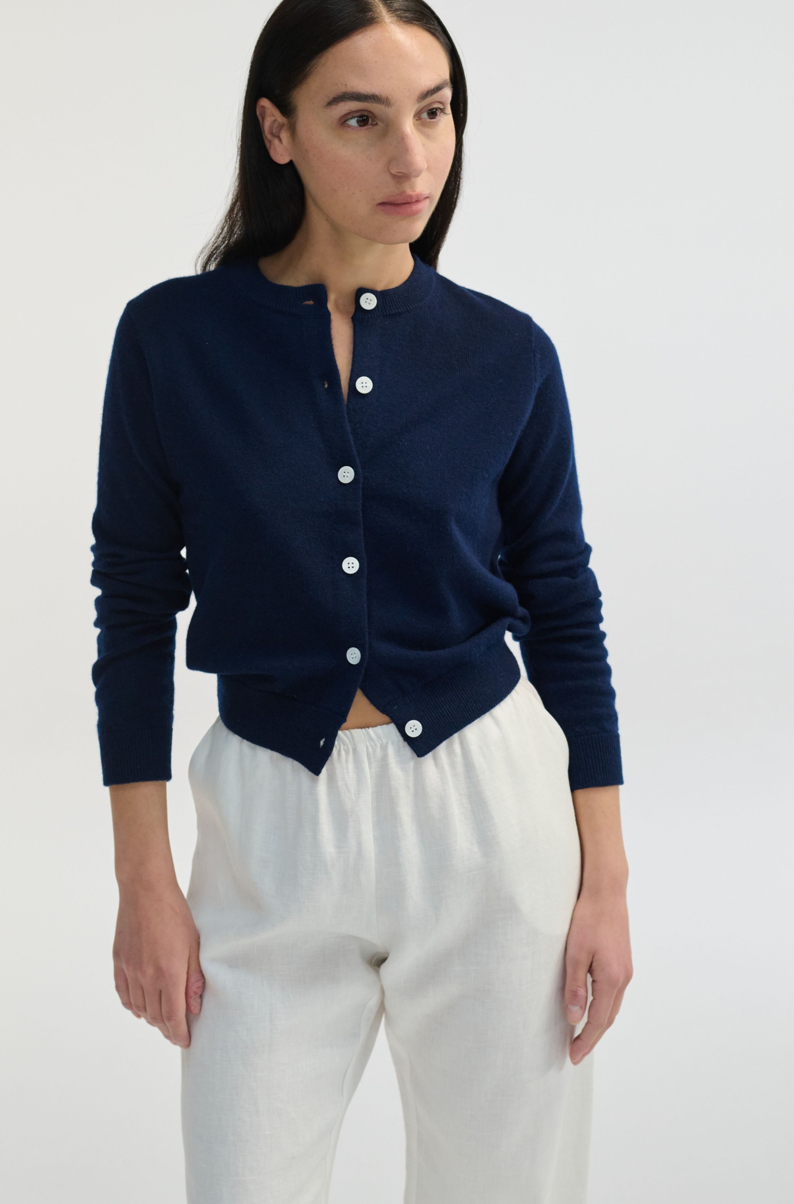 Woman wearing a navy blue cardigan with white buttons on a white background