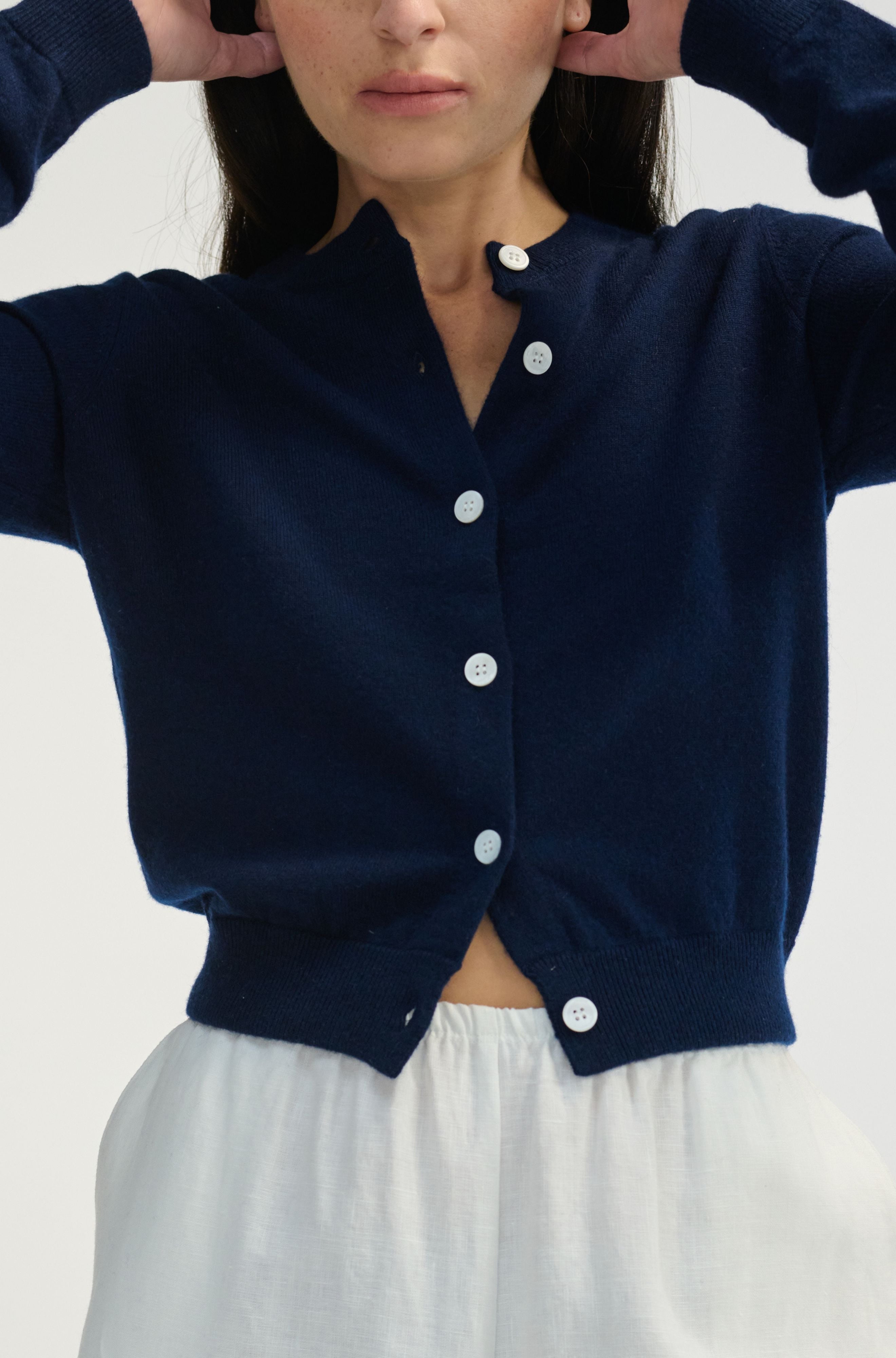 Woman wearing a navy blue cardigan with white buttons on a plain background