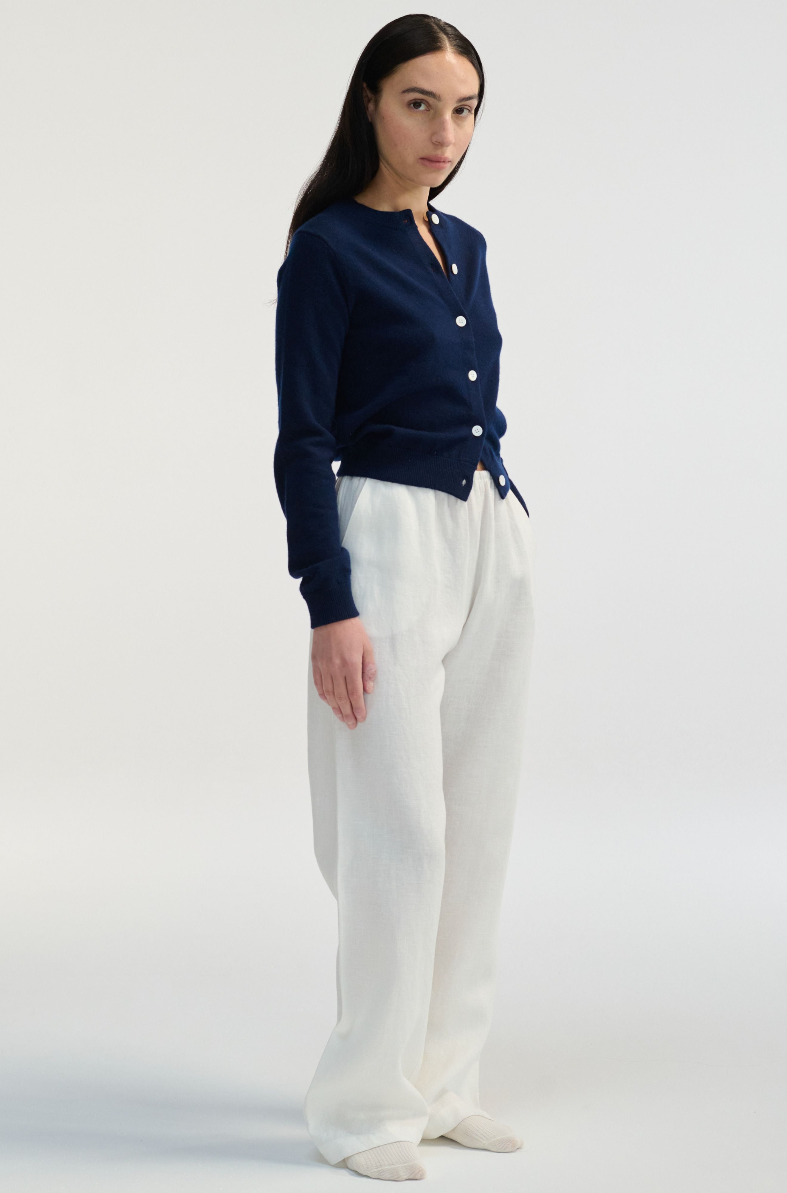 Woman wearing a navy blue cardigan and white pants on a light gray background