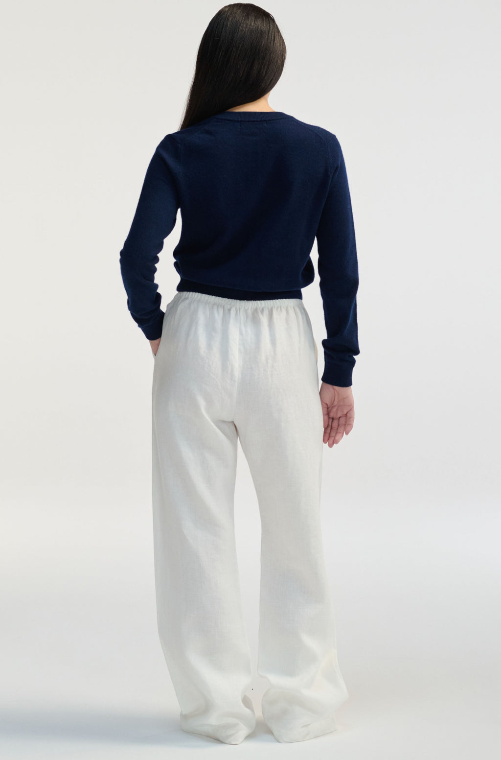 Person wearing a navy sweater and white pants on a light gray background