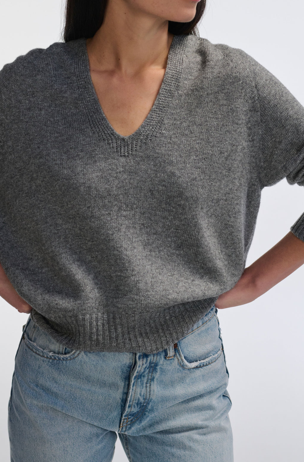Person wearing a gray sweater and blue jeans on a white background