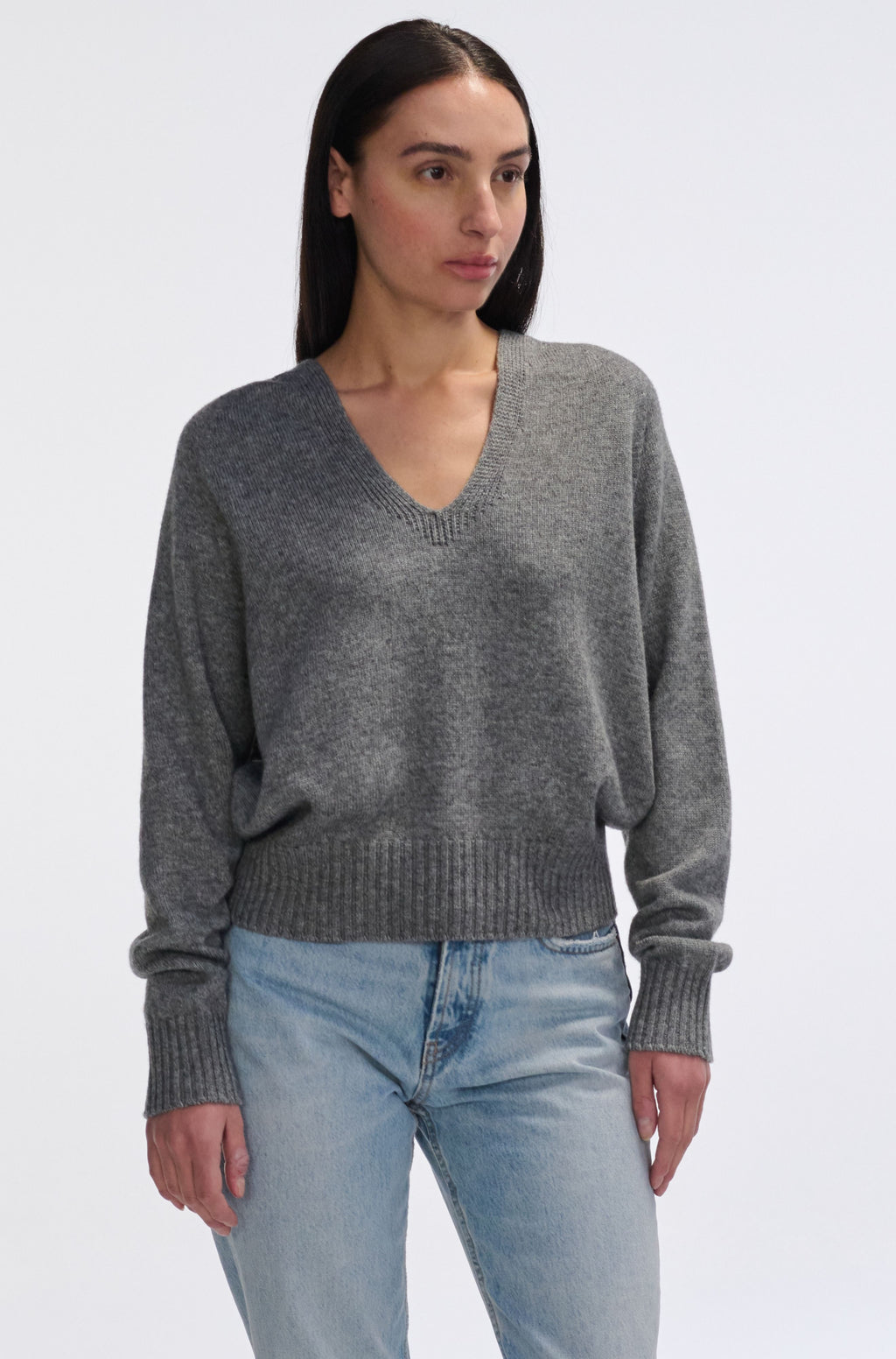 Woman wearing a gray sweater and light blue jeans on a white background