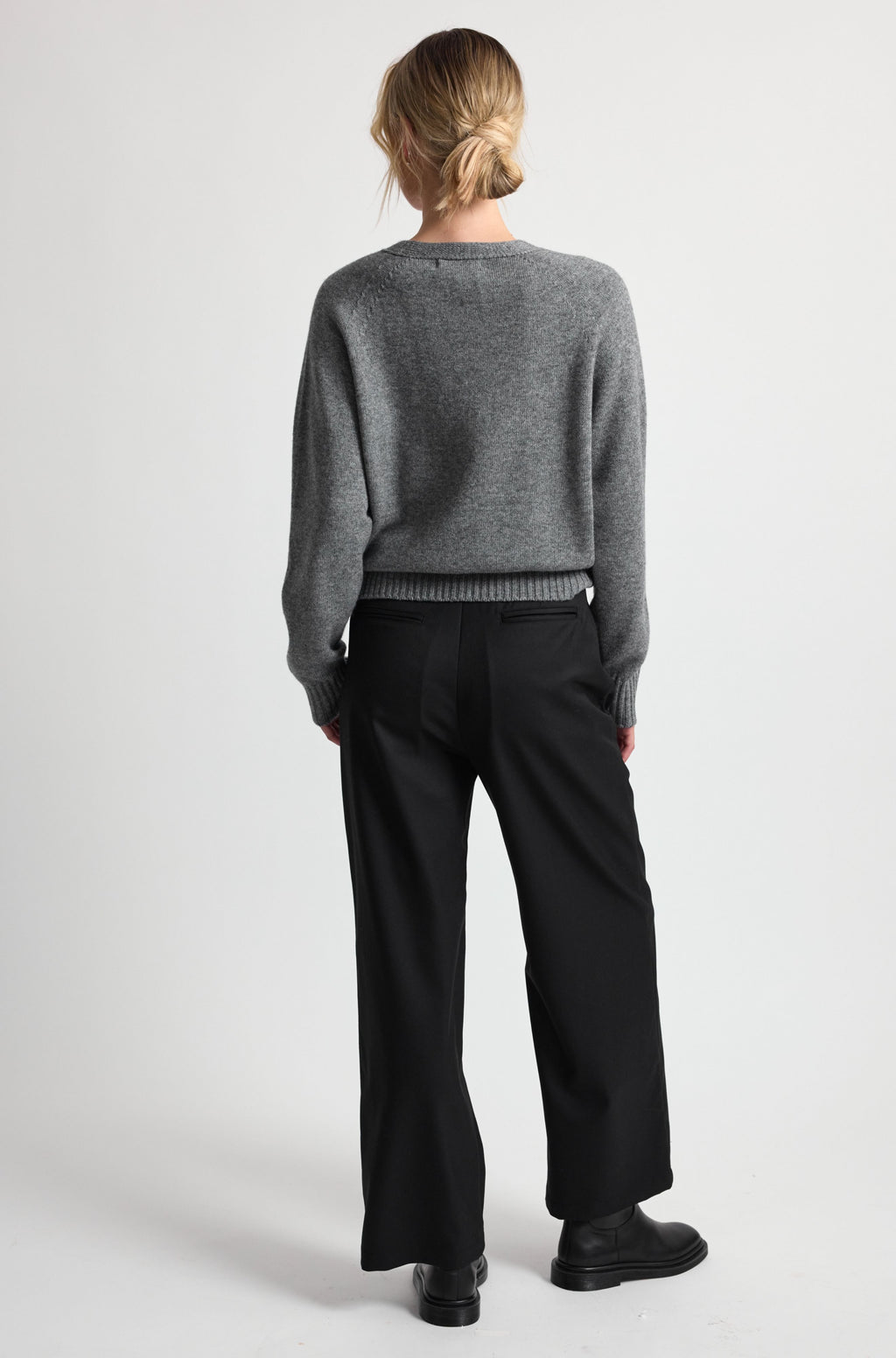 Person wearing a gray sweater and black pants on a white background