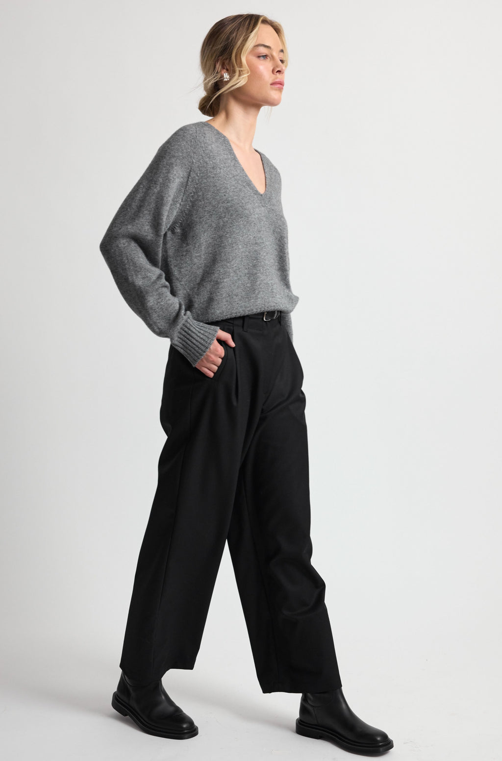 Woman wearing a gray sweater and black pants on a white background