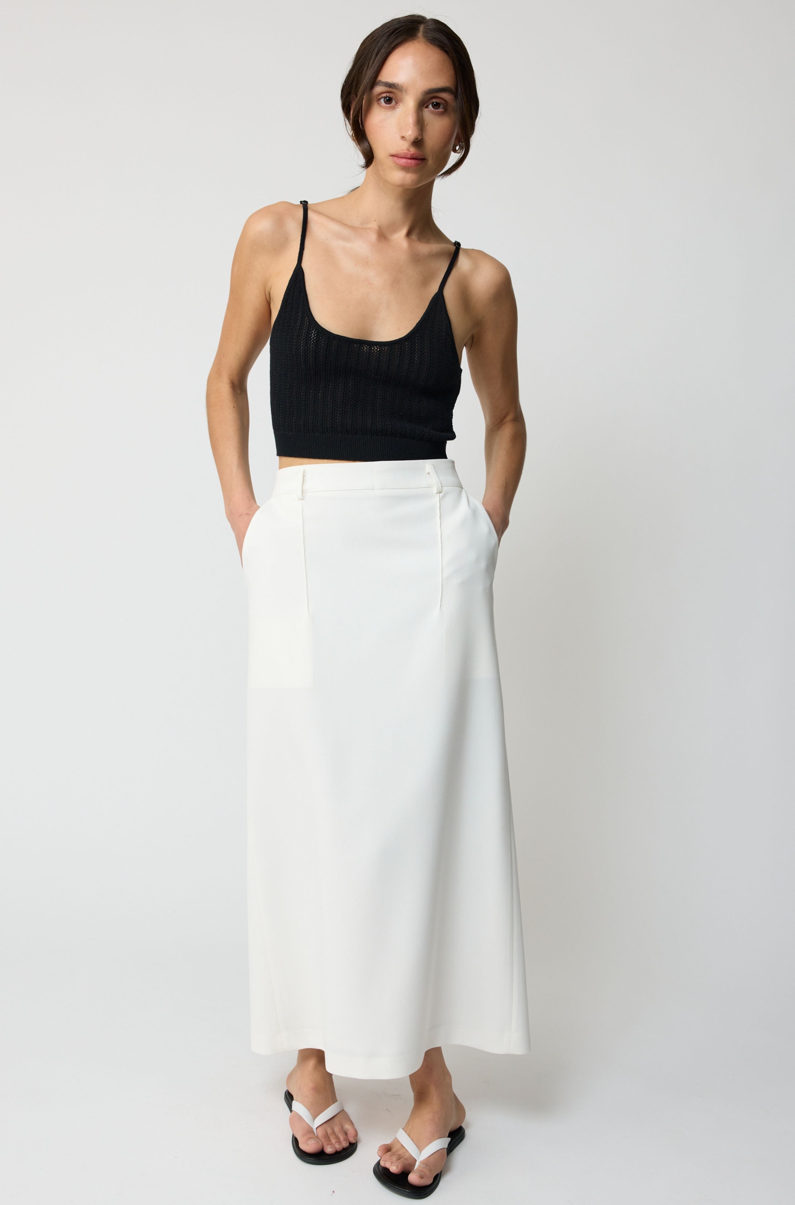 Woman wearing a black tank top and white skirt on a plain background
