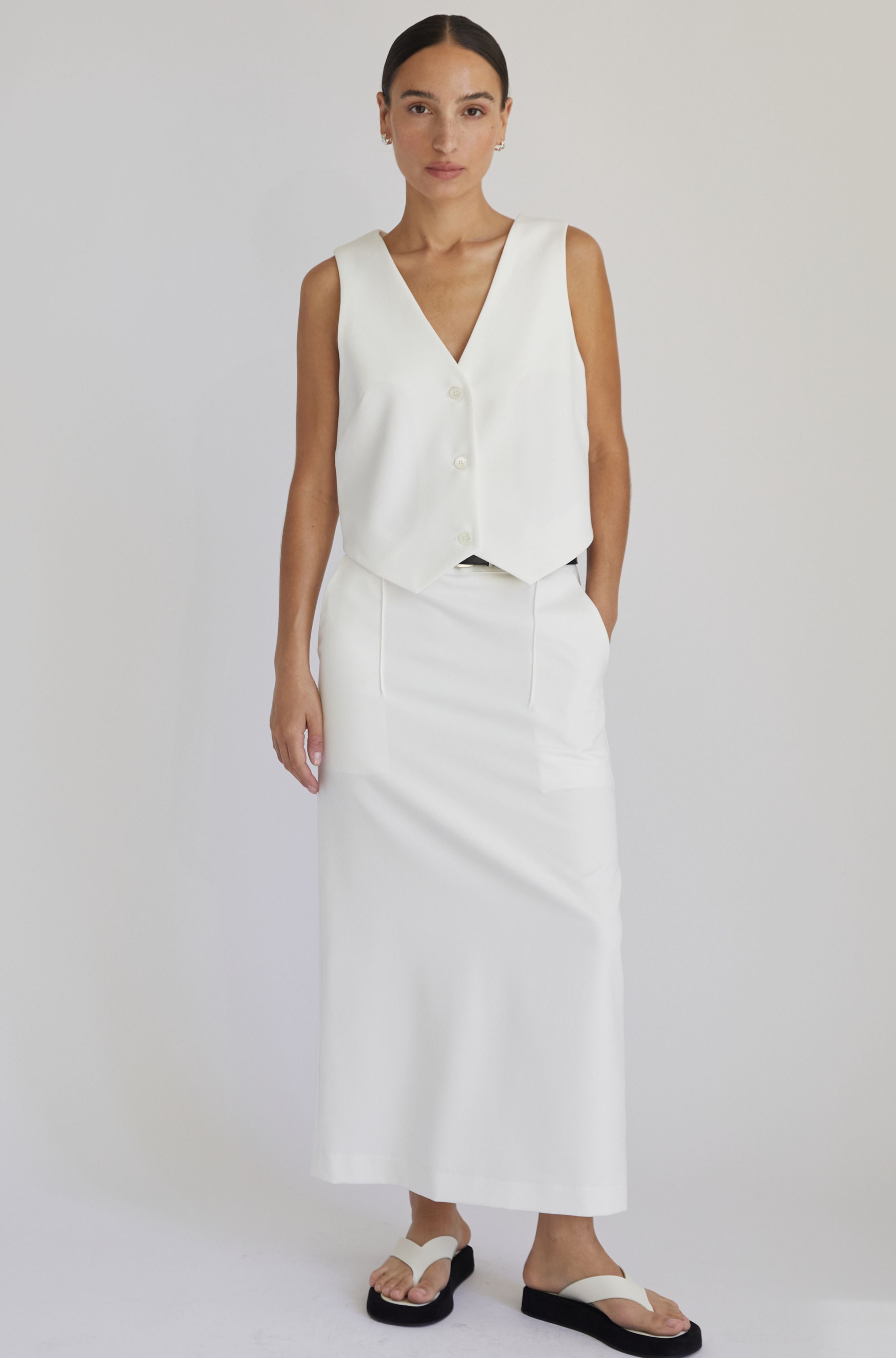 Woman wearing a white sleeveless top and skirt set on a plain background