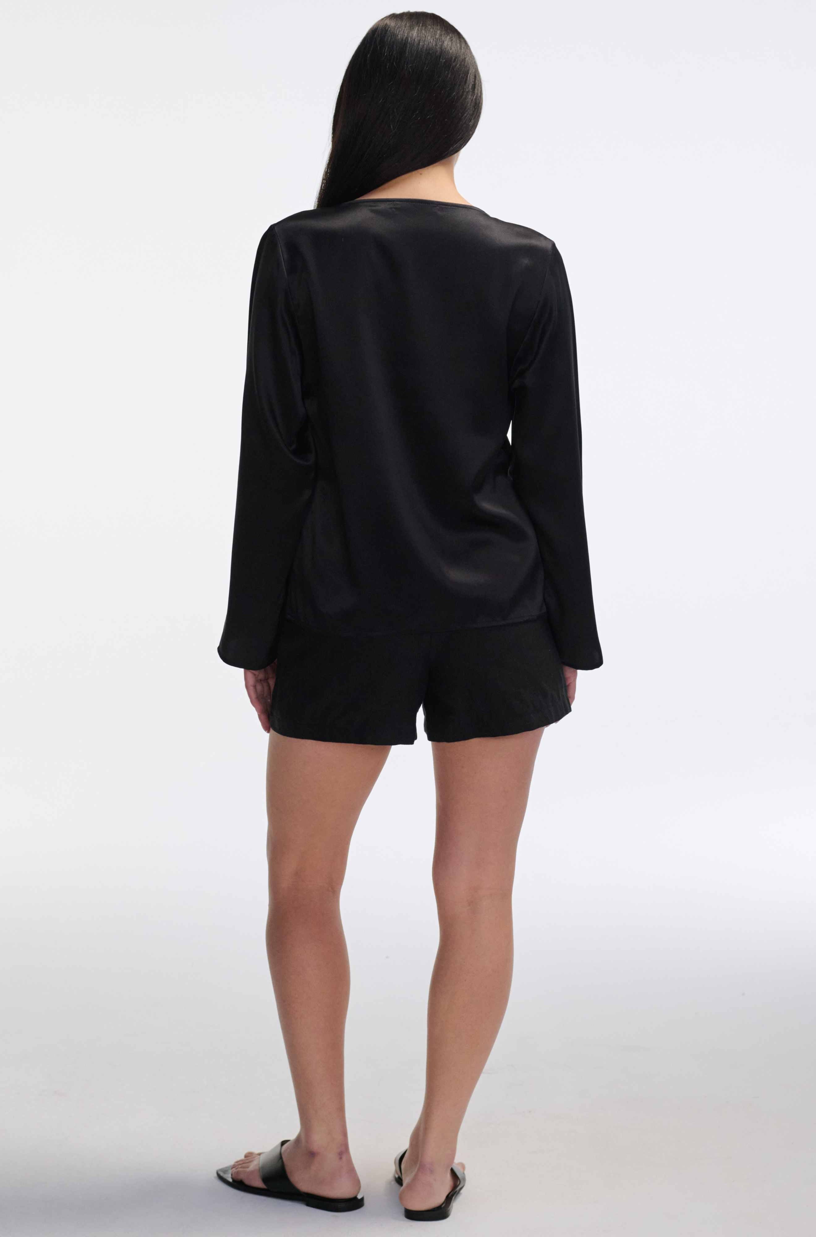 Person wearing a black silk shirt with long sleeves and shorts on a white background