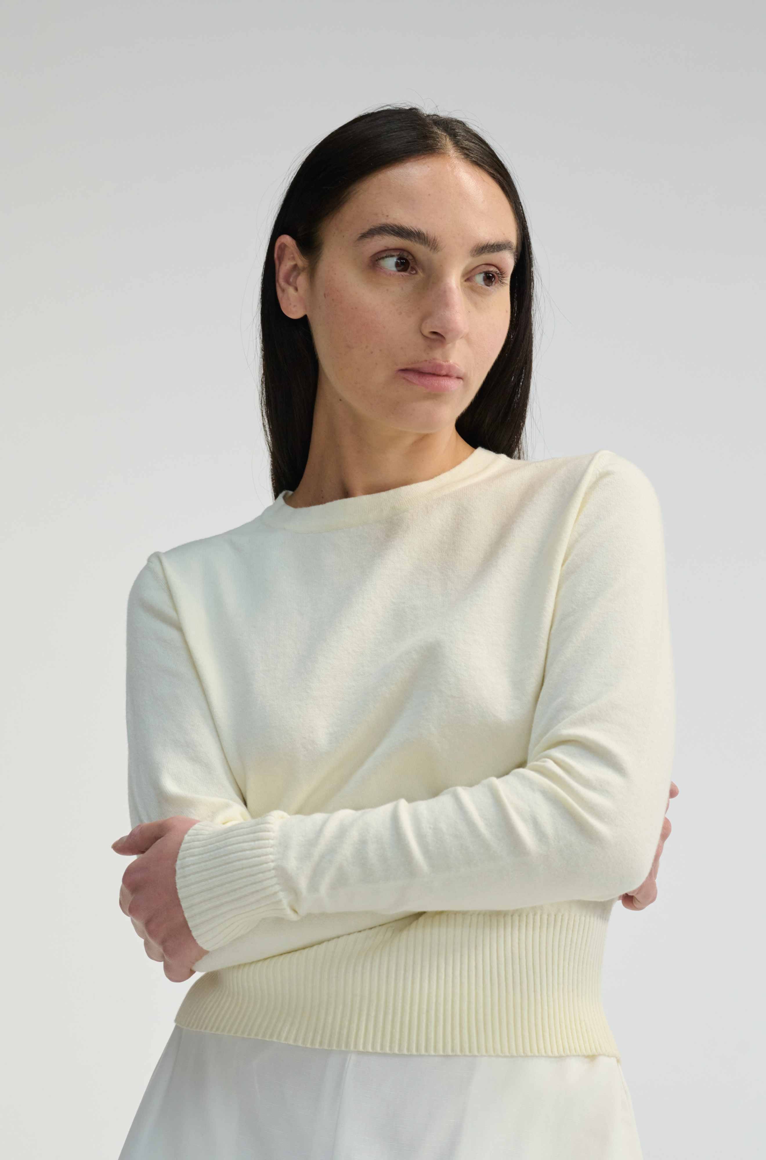 Woman wearing an ivory long sleeve sweater against a plain background
