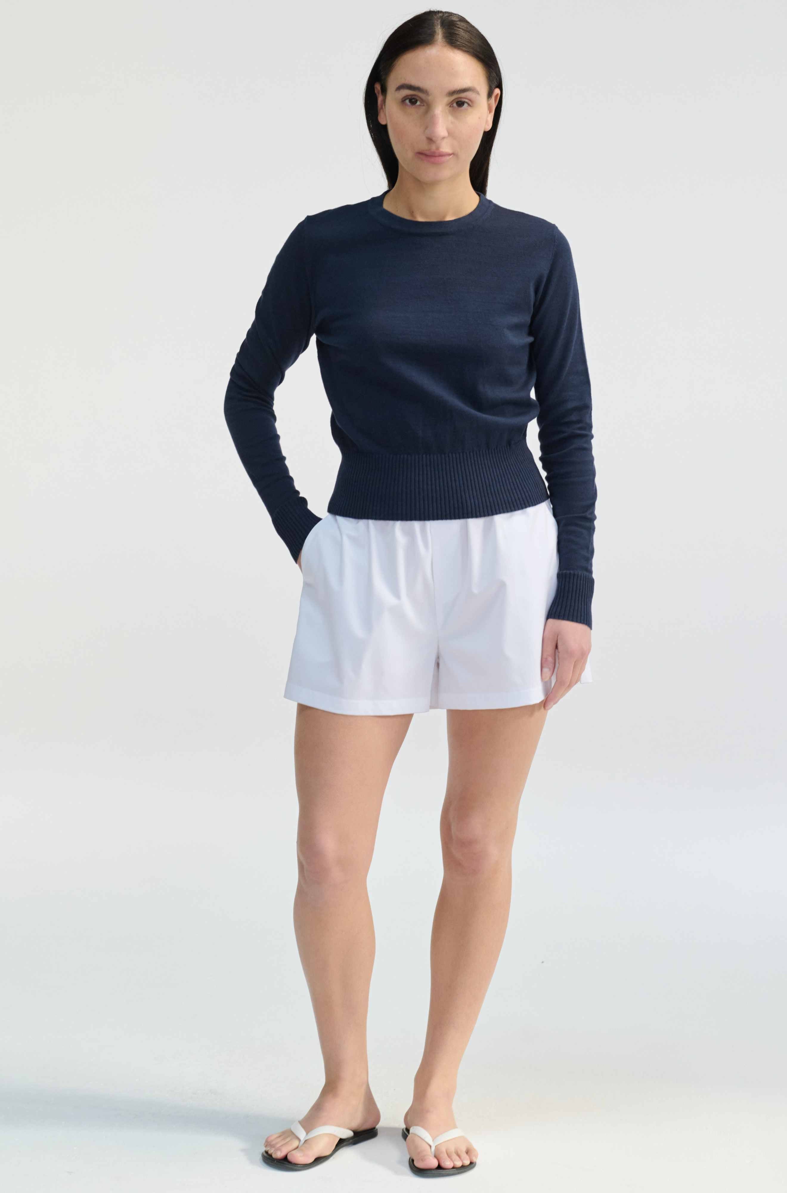 Woman wearing a navy sweater and white shorts on a plain background