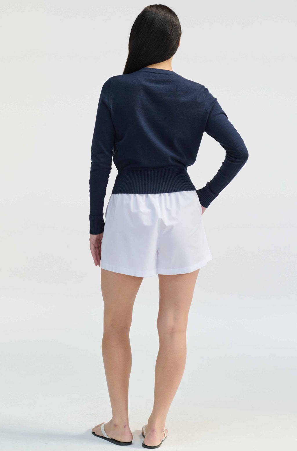 Person wearing a navy sweater and white shorts on a light gray background