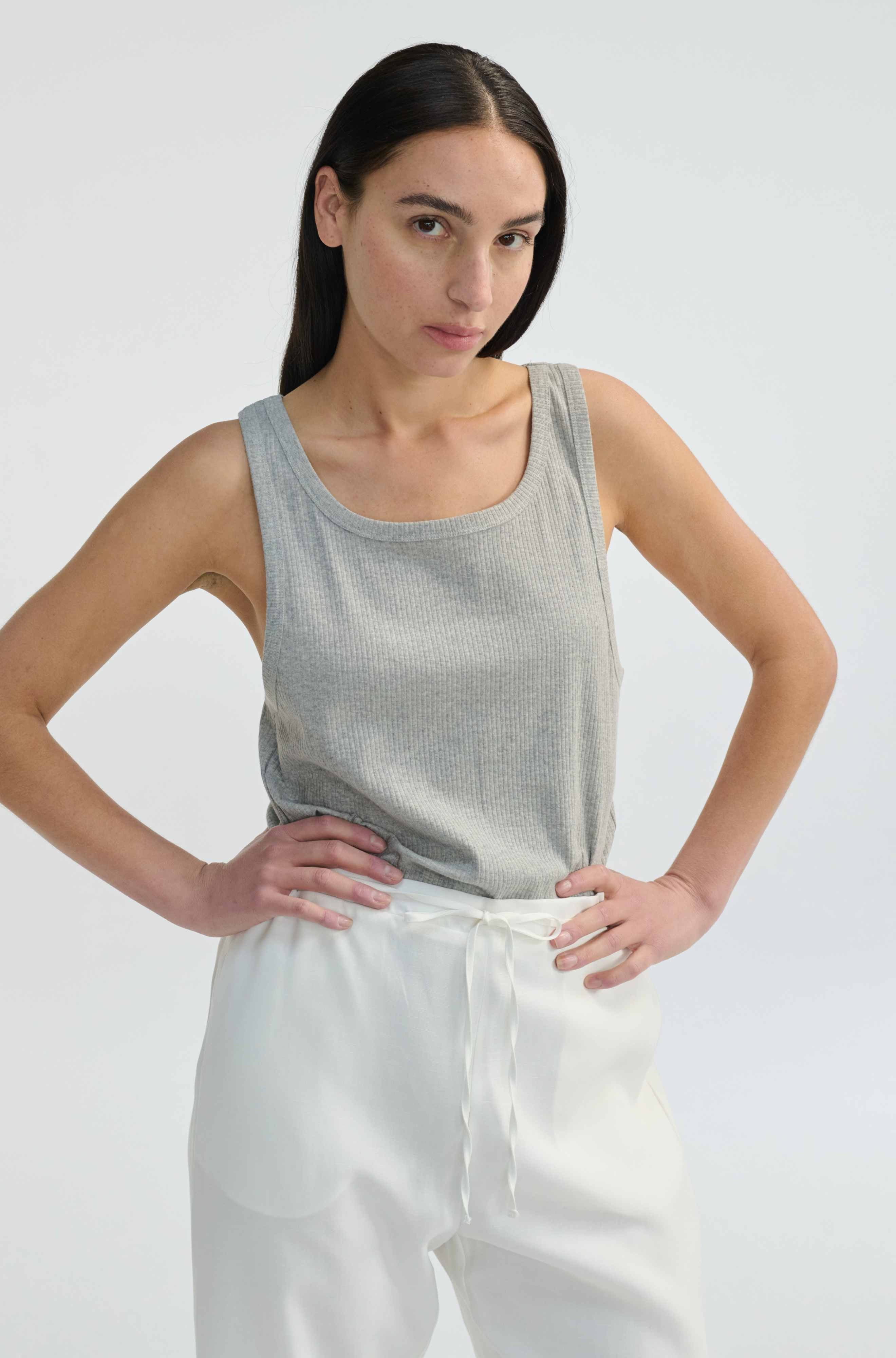 Woman wearing a gray tank top and white pants against a plain background