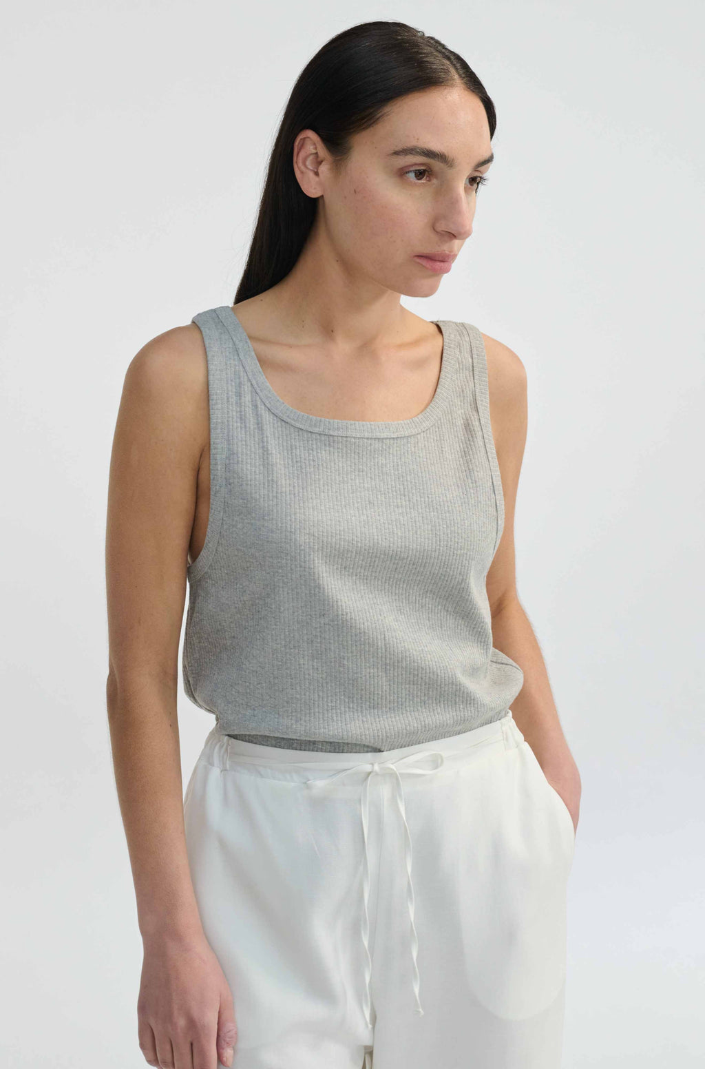 Woman wearing a gray tank top and white pants against a plain background