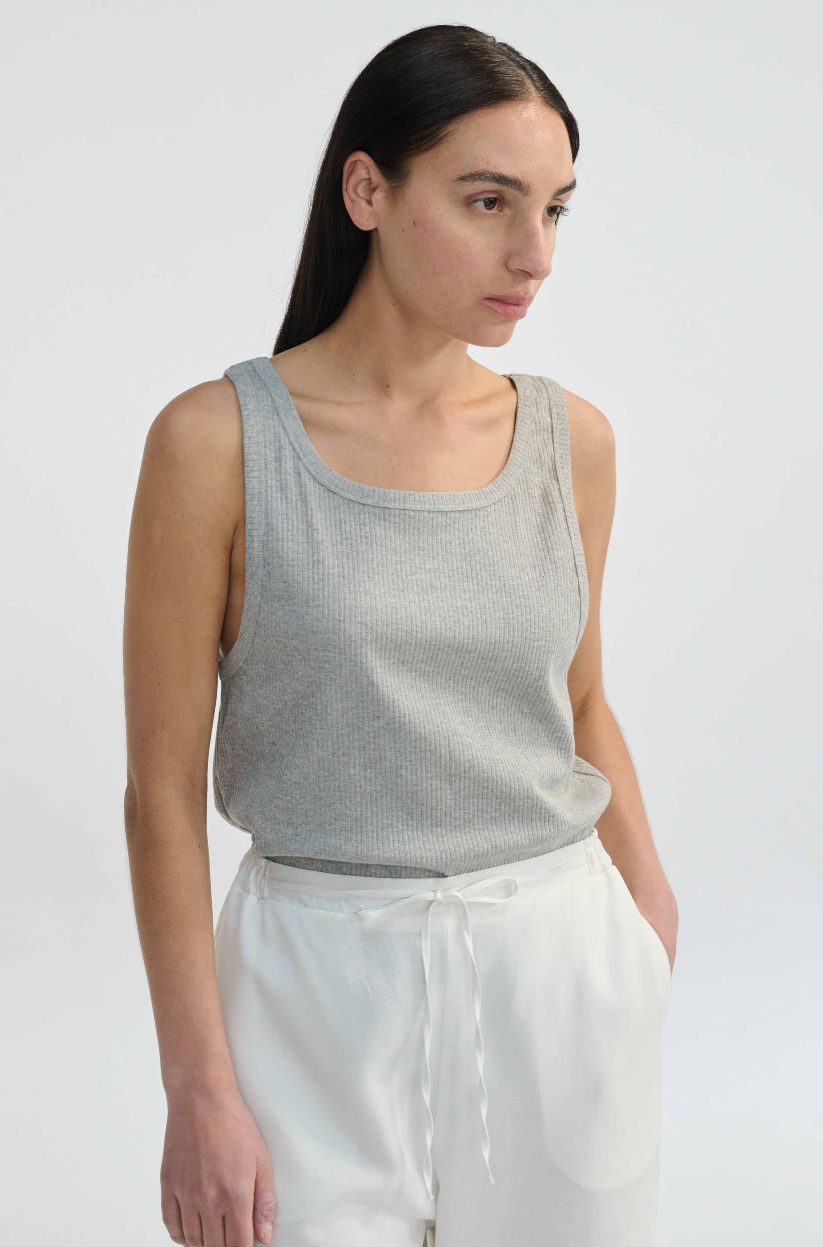Woman wearing a gray tank top and white pants against a plain background
