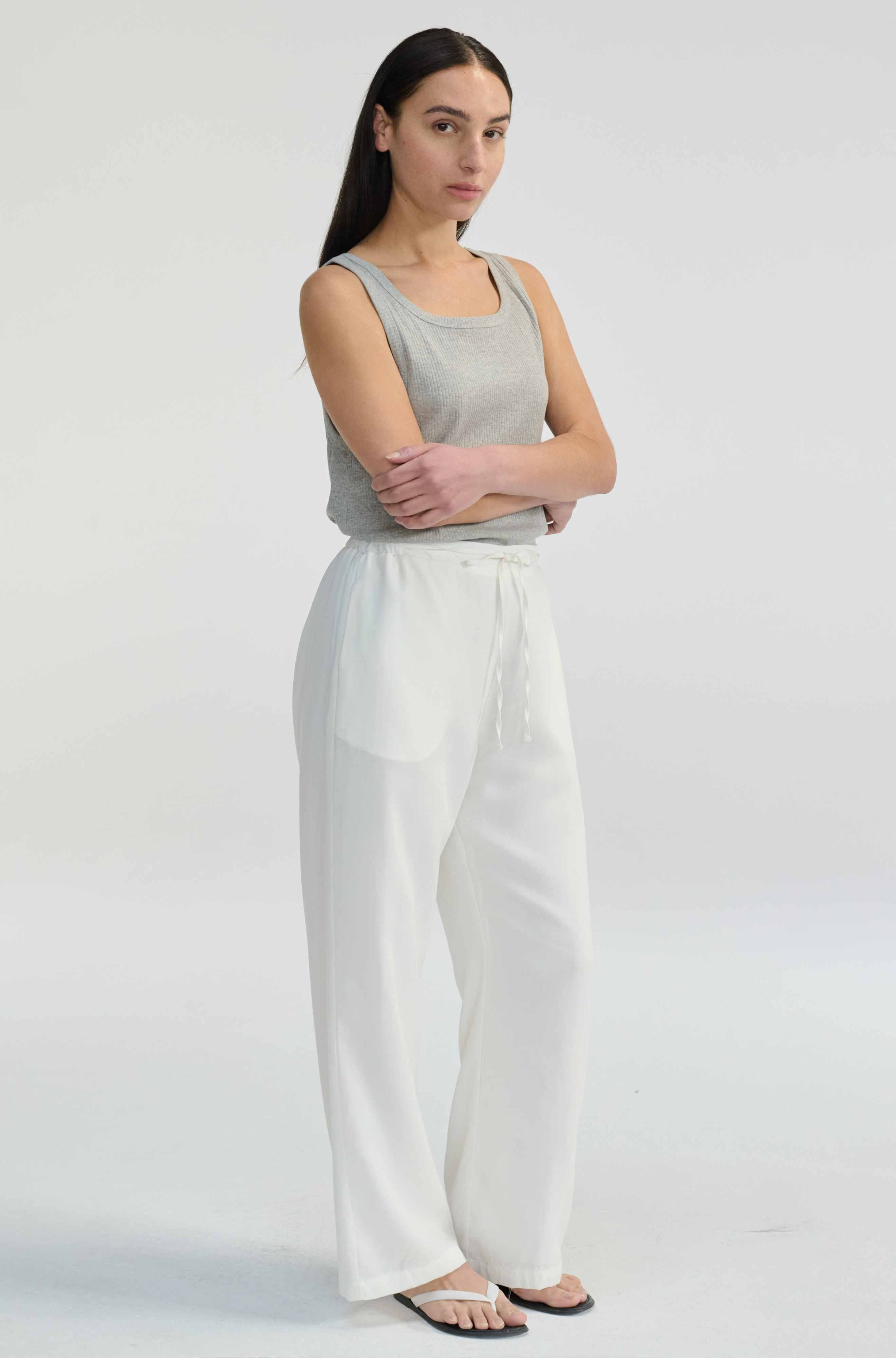 Woman wearing a gray sleeveless top and white pants on a light gray background