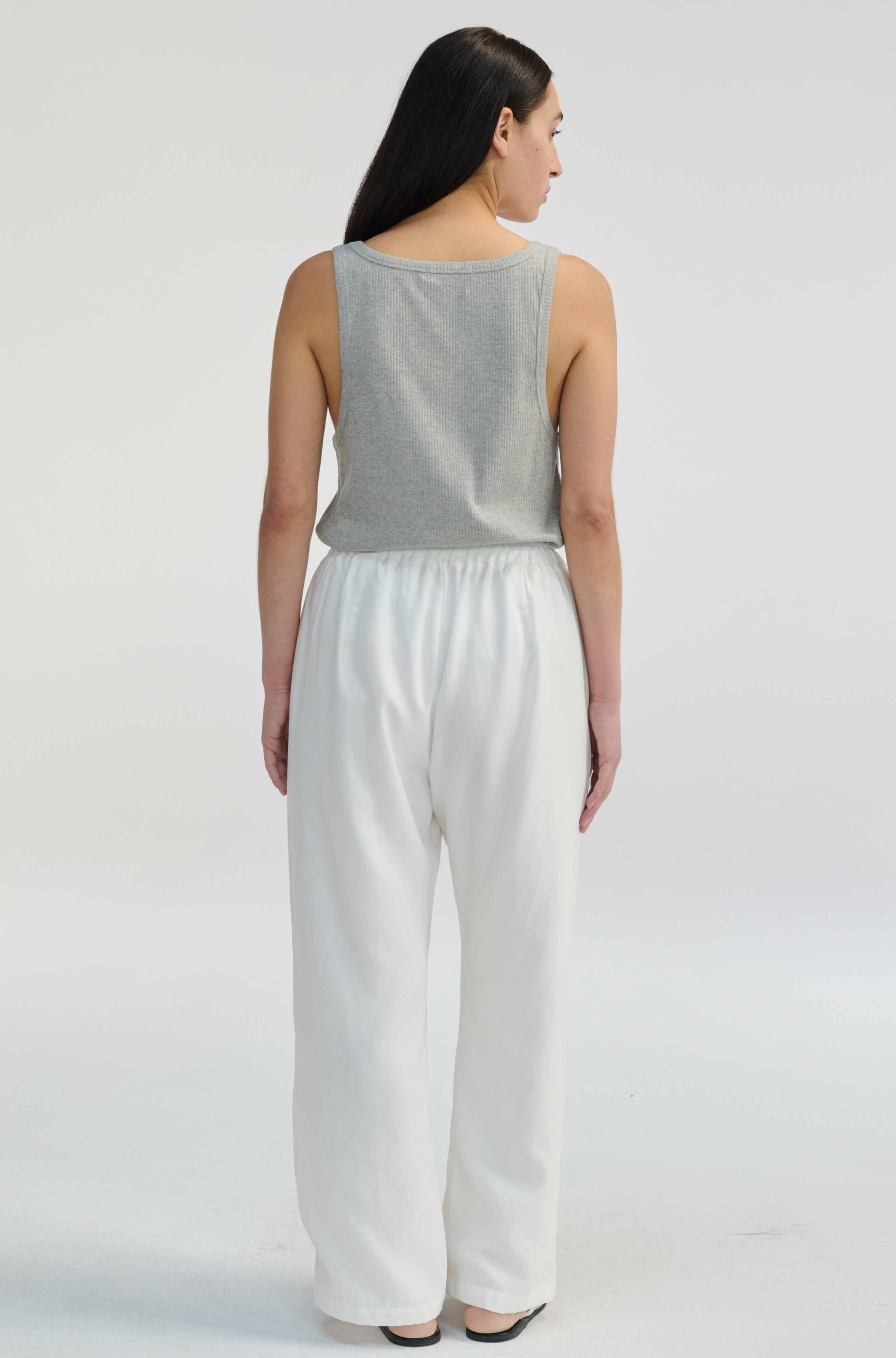 Woman wearing a gray sleeveless top and white pants on a plain background