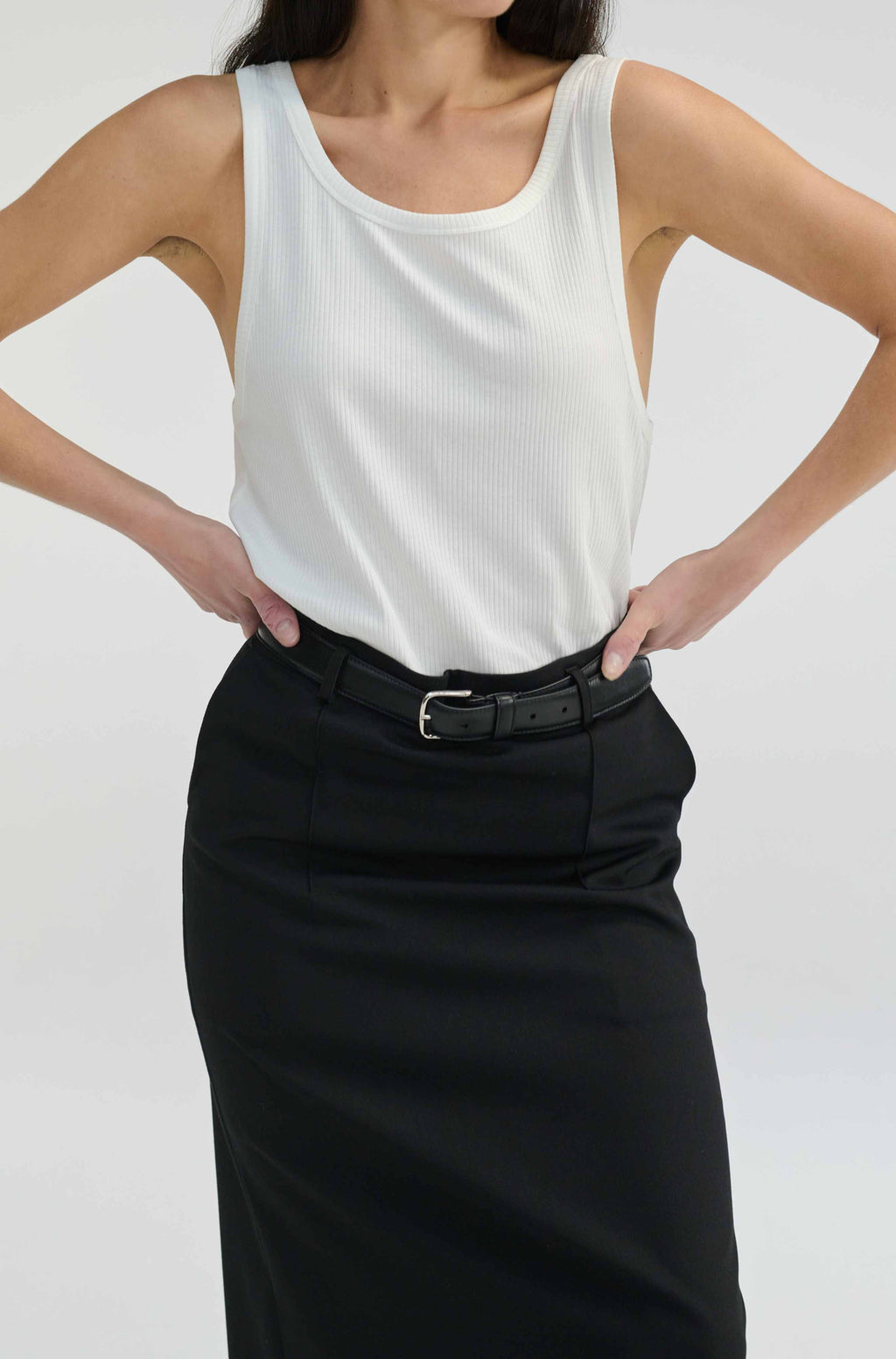 Person wearing a white sleeveless top and black skirt on a plain background