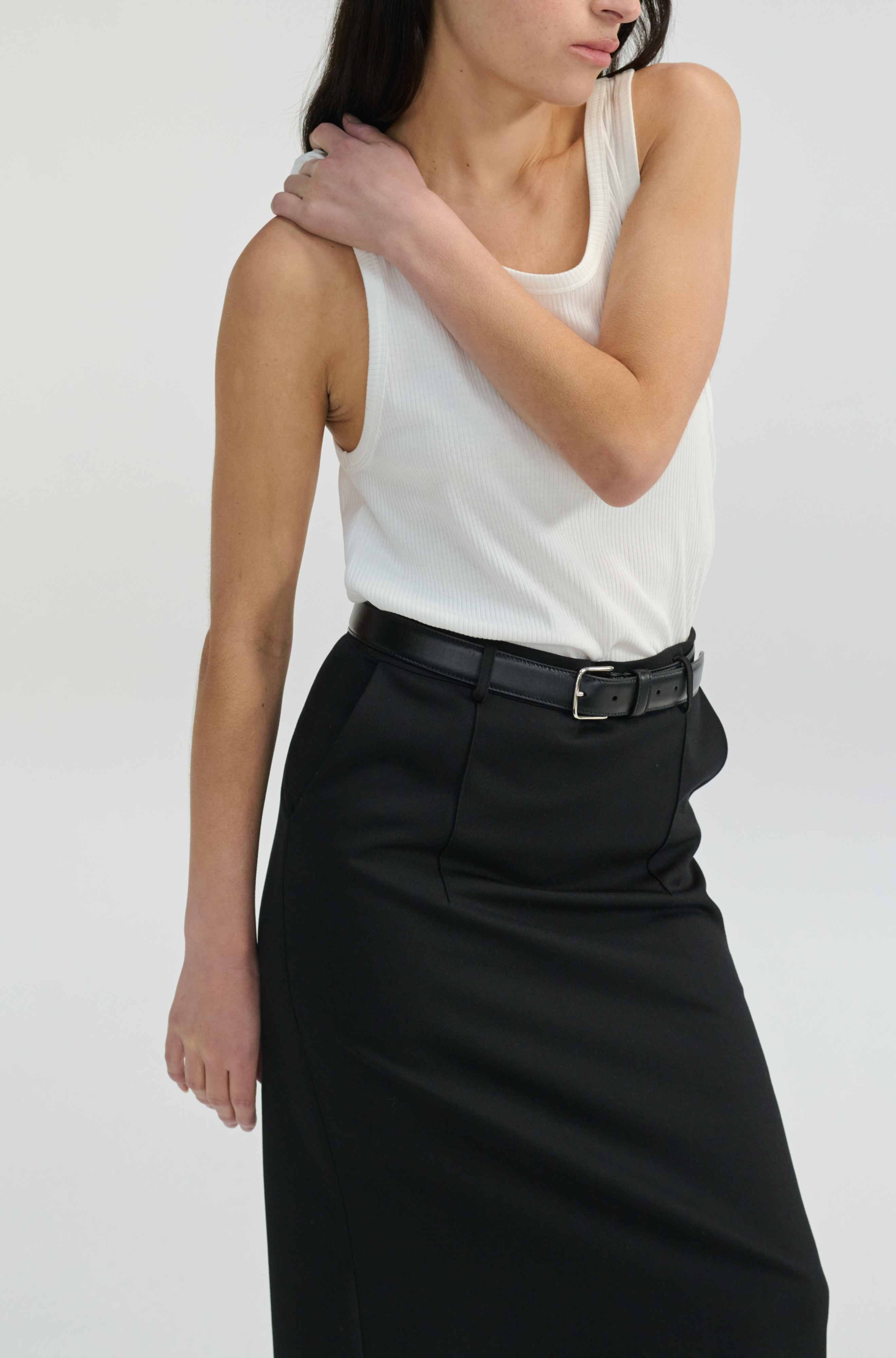 Woman wearing a white tank top and black skirt on a plain background