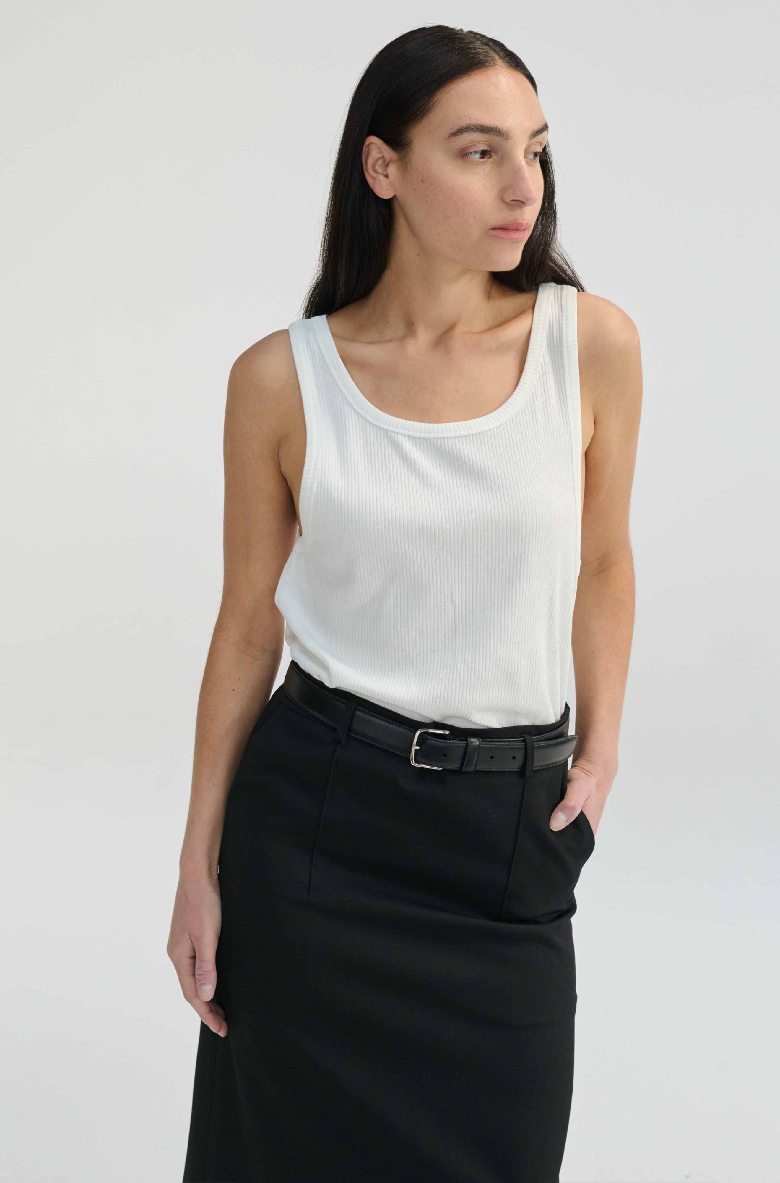 Woman wearing a white sleeveless top and black skirt on a plain background
