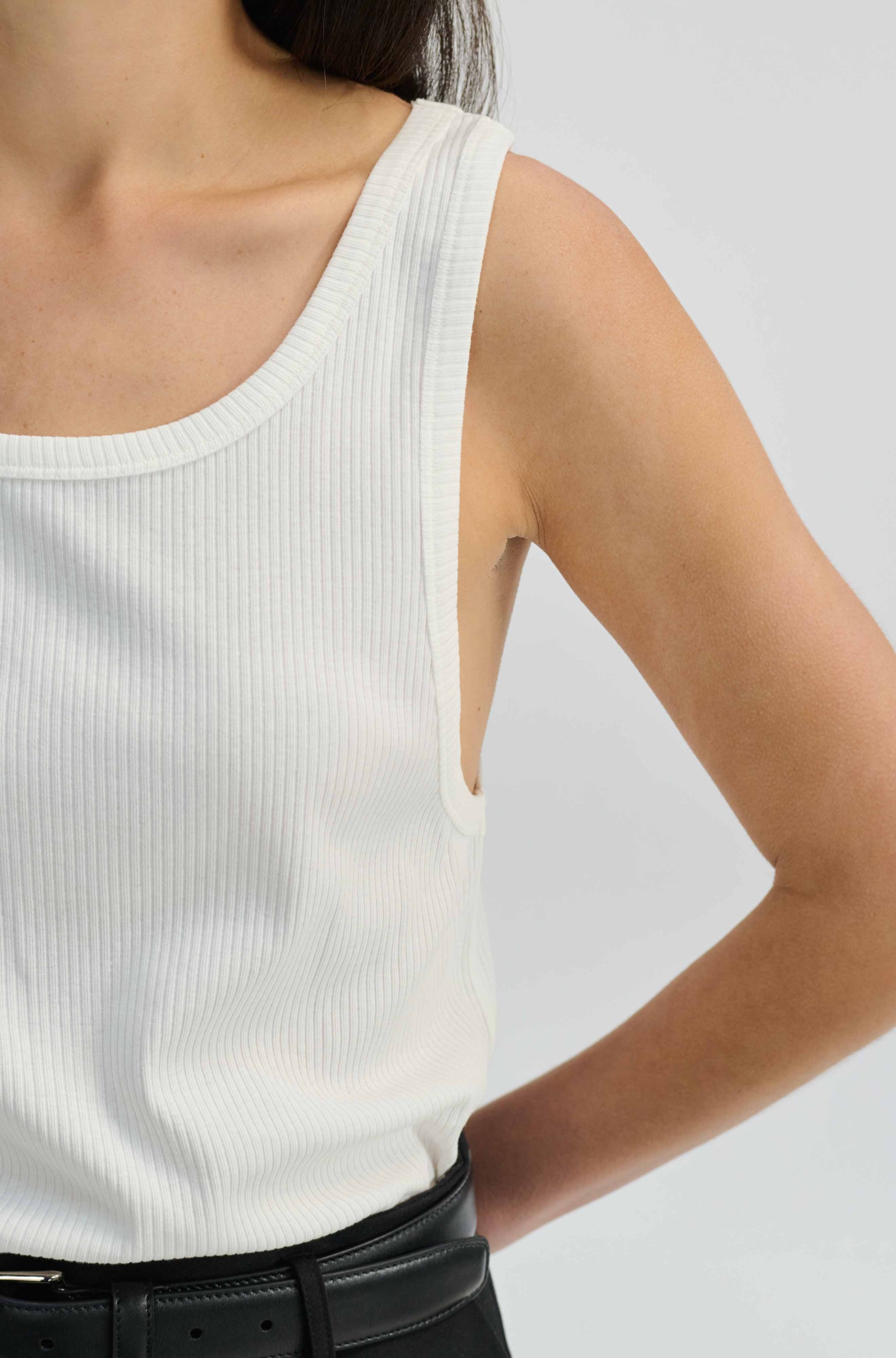 Person wearing a white ribbed tank top and black skirt on a light gray background