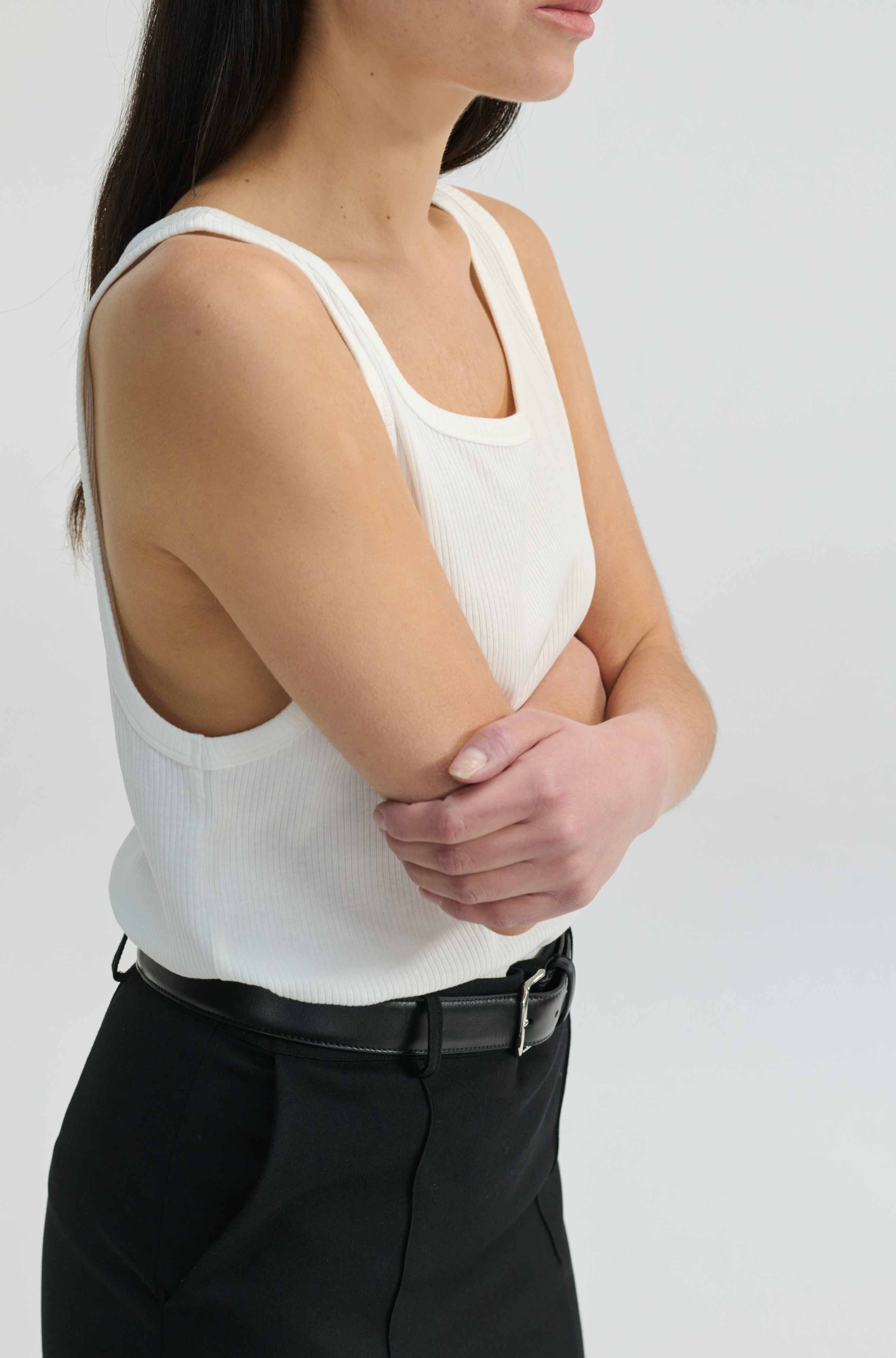Person wearing a white sleeveless top and black skirt on a plain background