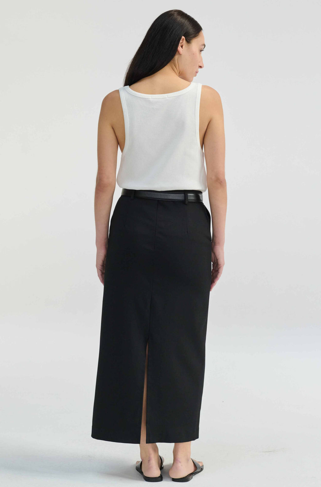 Woman wearing a white sleeveless top and black skirt on a plain background