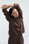 Woman wearing a brown outfit with long sleeves and pants against a white background