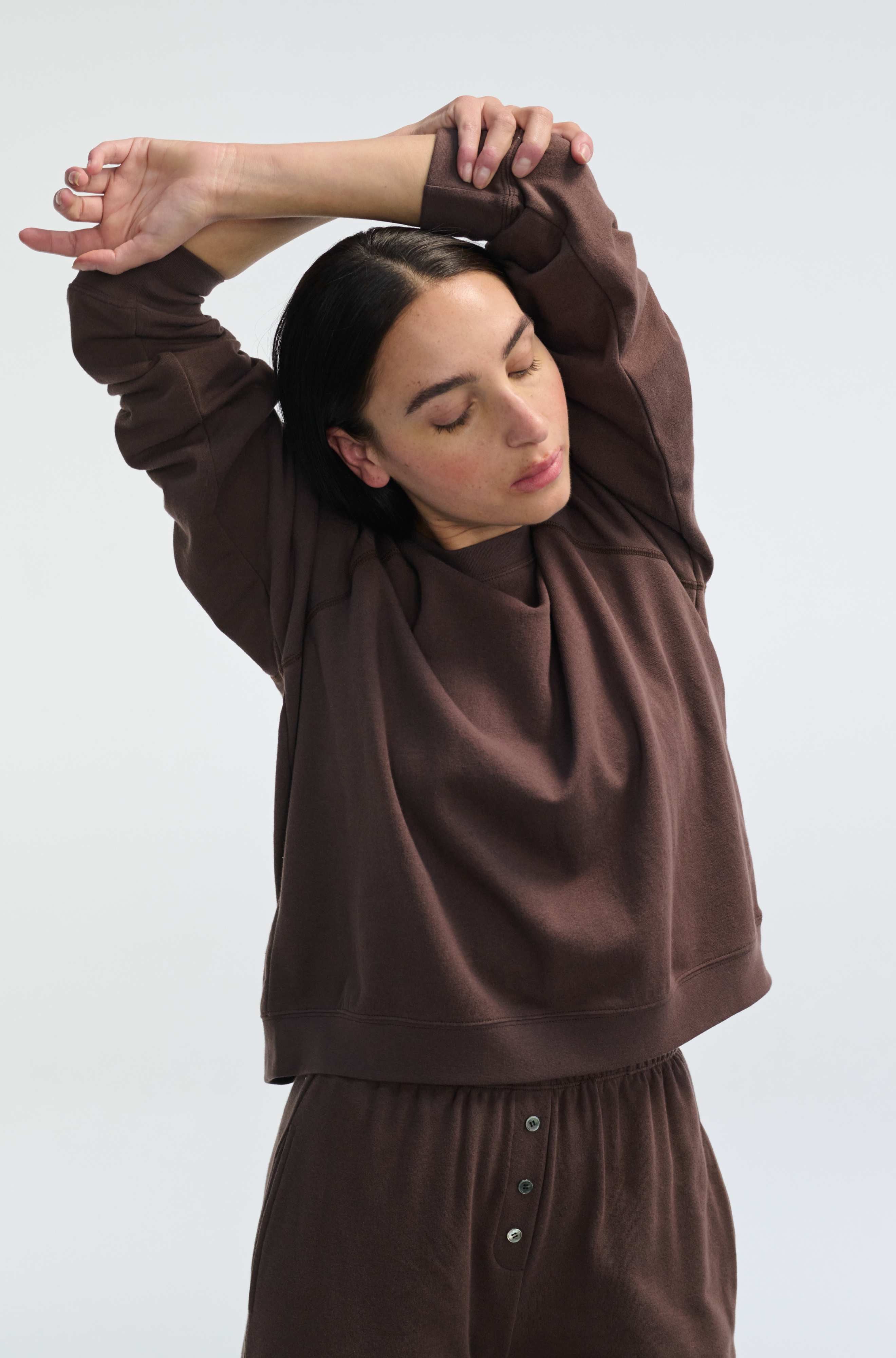 Woman wearing a brown outfit with long sleeves and pants against a white background