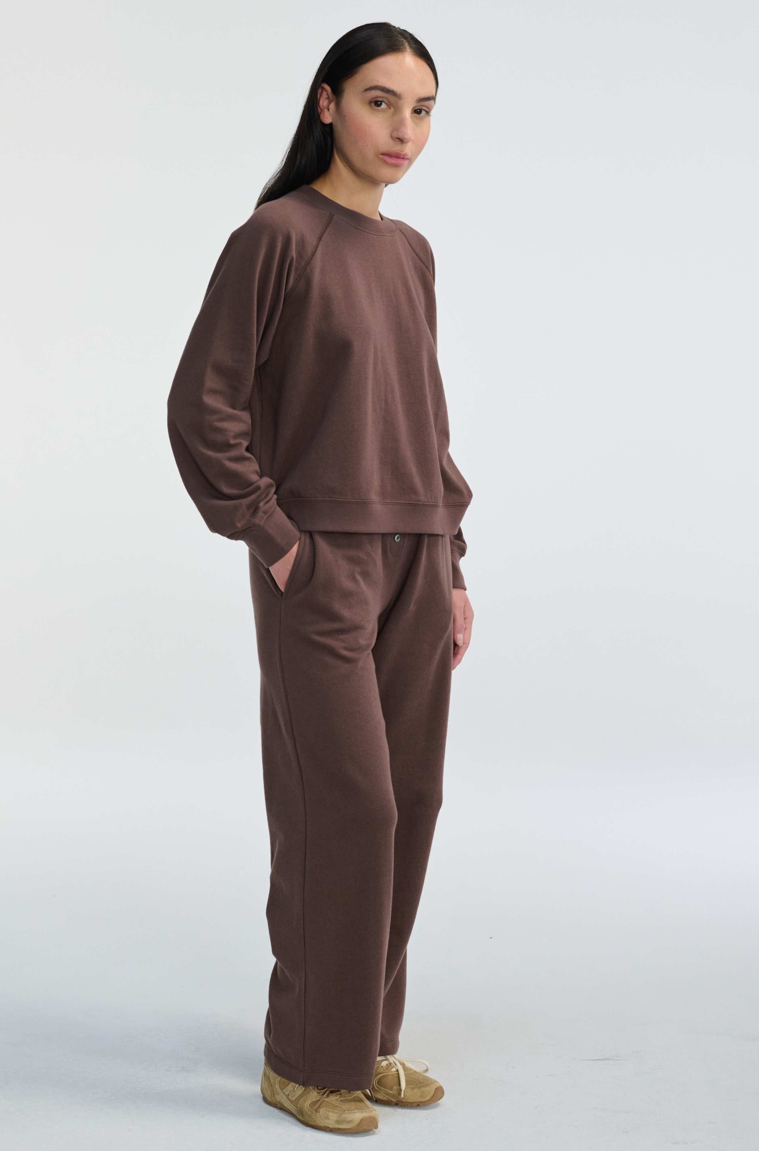 Person wearing a brown sweatshirt and pants on a white background