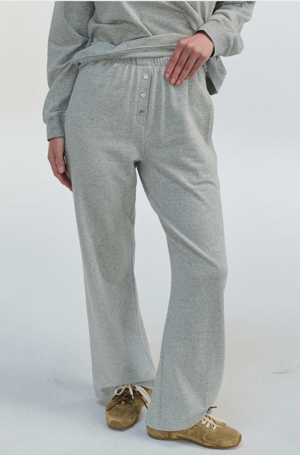 Woman wearing grey sweatpants with buttons up the front on a grey background