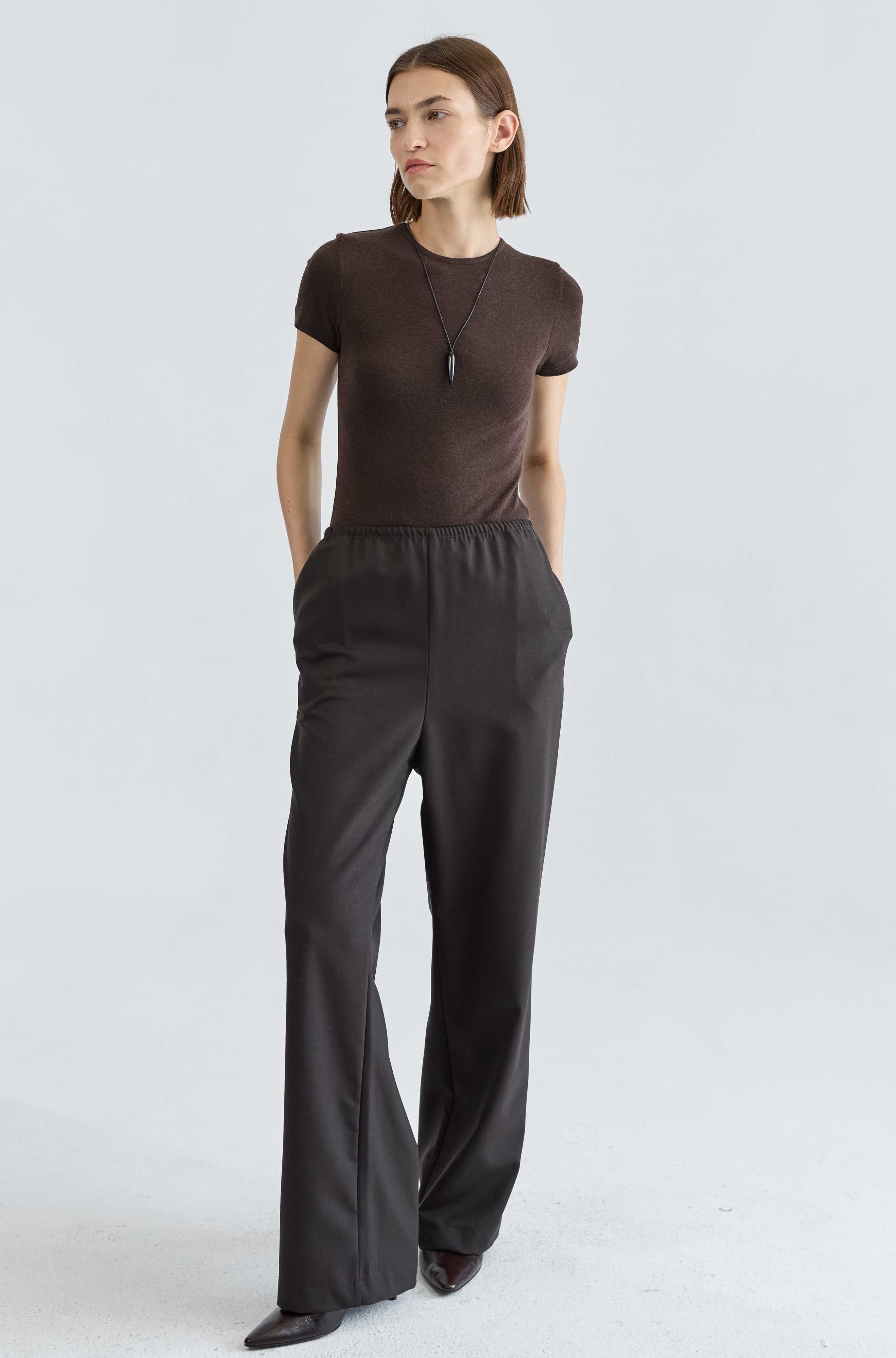 Woman wearing a brown top and dark brown pants on a white background