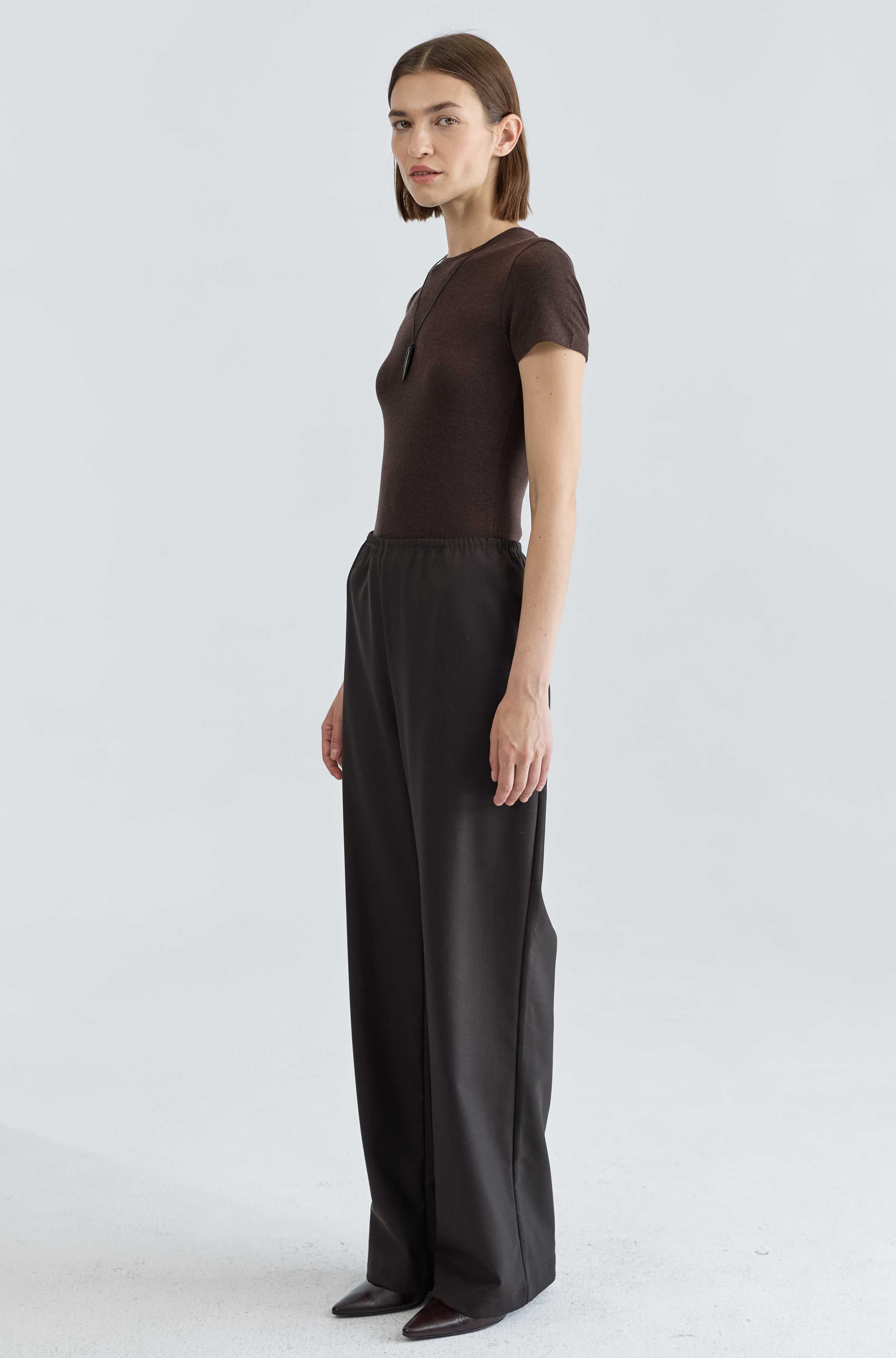 Person wearing a brown top and dark brown pants on a white background