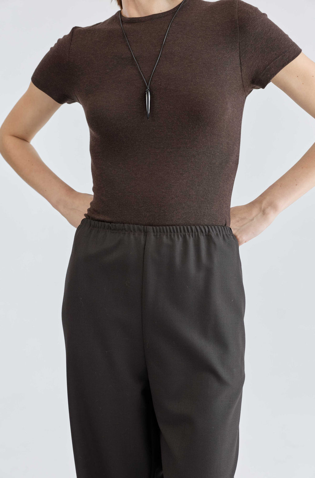 Person wearing a brown t-shirt and dark pants on a white background