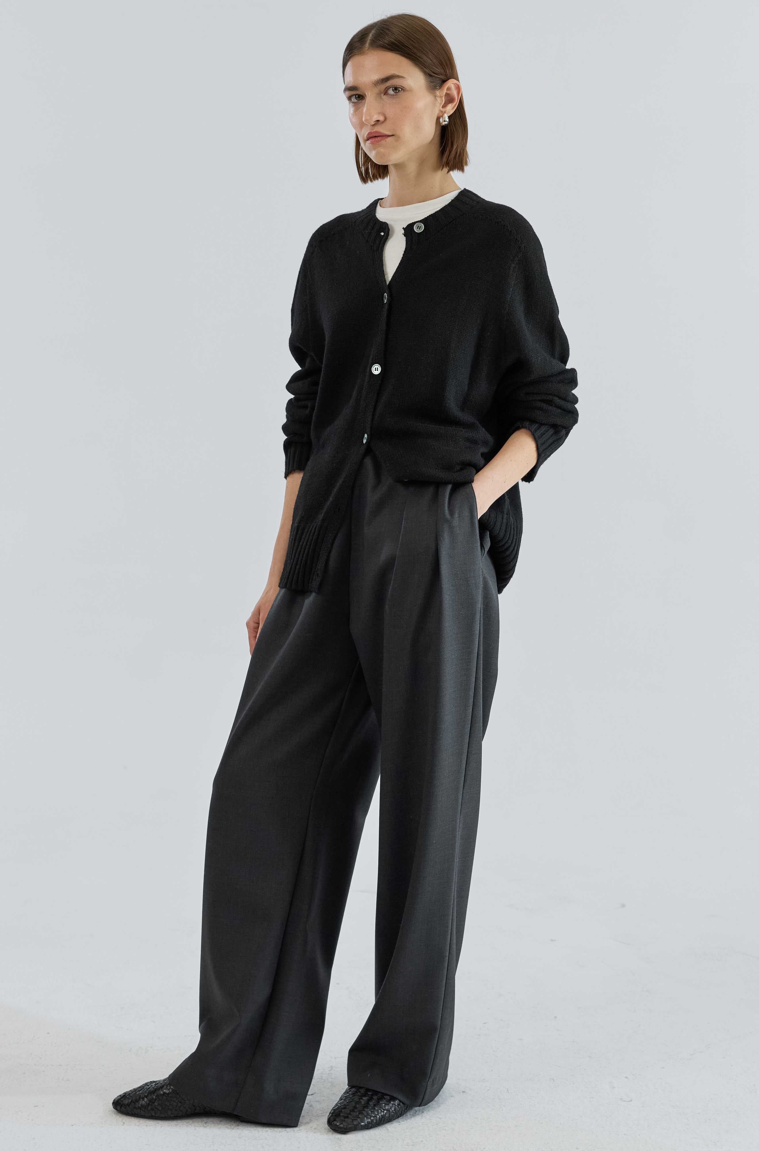 Person wearing a black cardigan and wide-leg pants on a white background