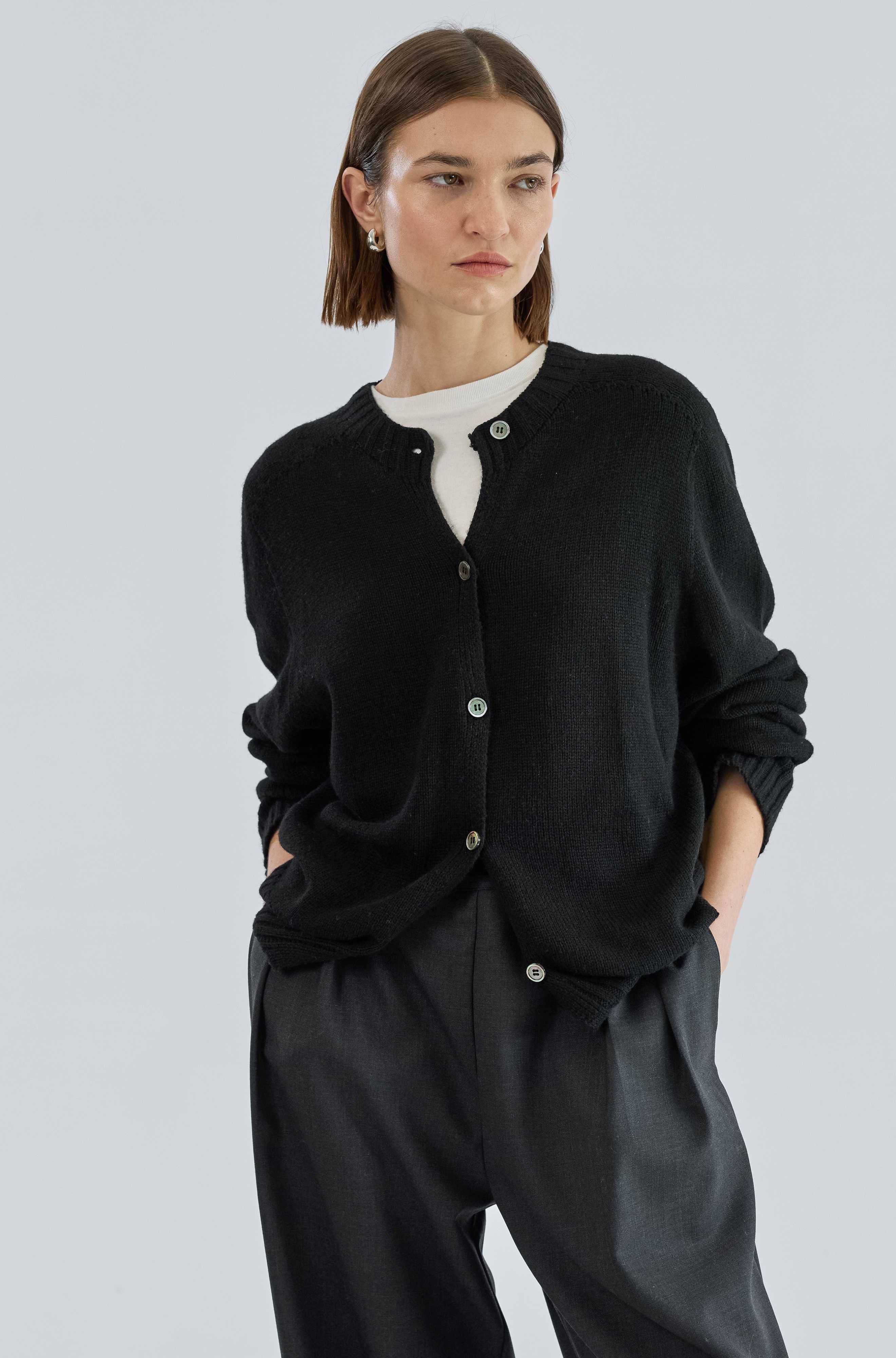 Person wearing a black cardigan and dark pants on a light gray background