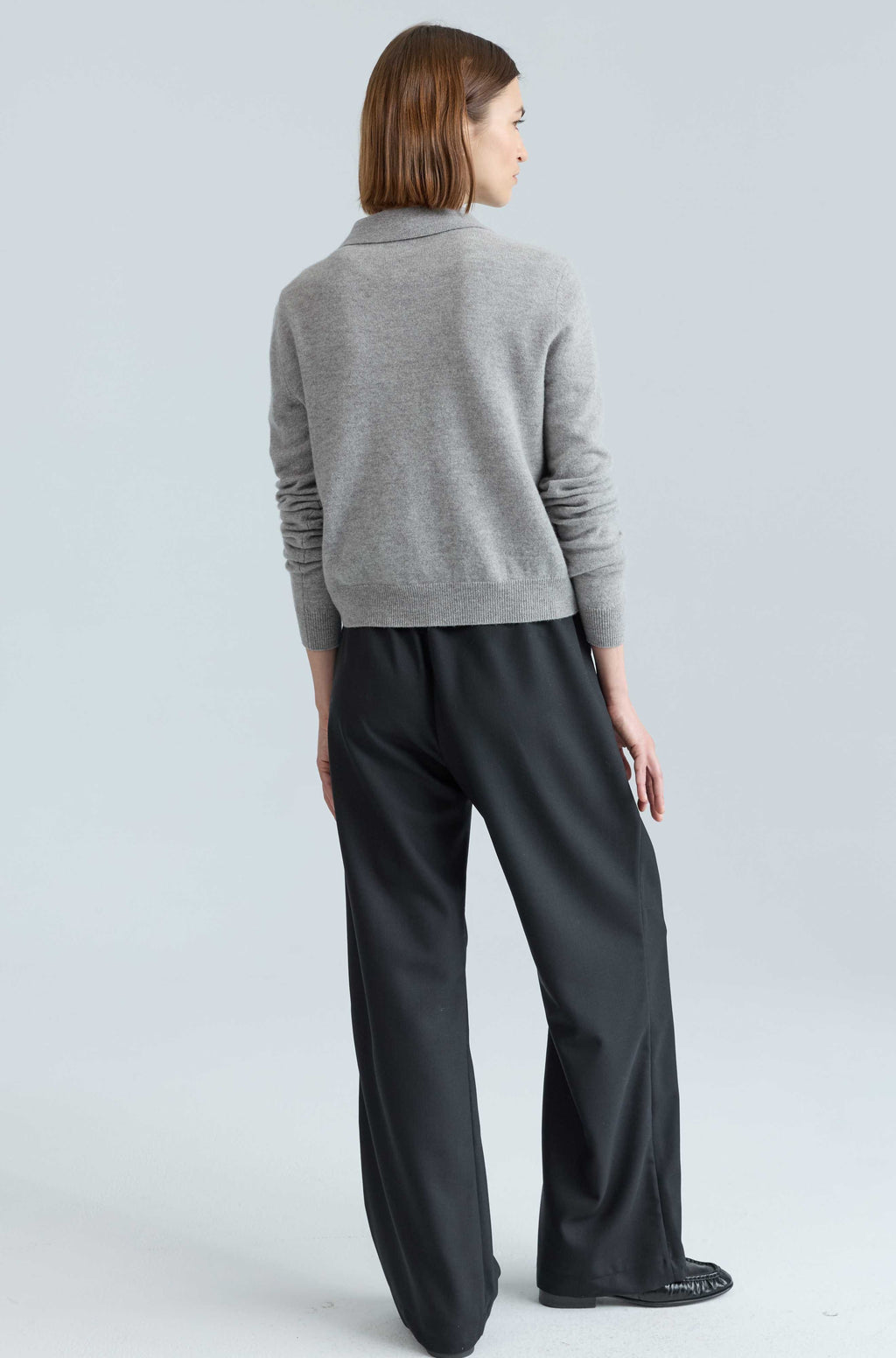 Woman wearing a gray sweater and black pants on a light gray background
