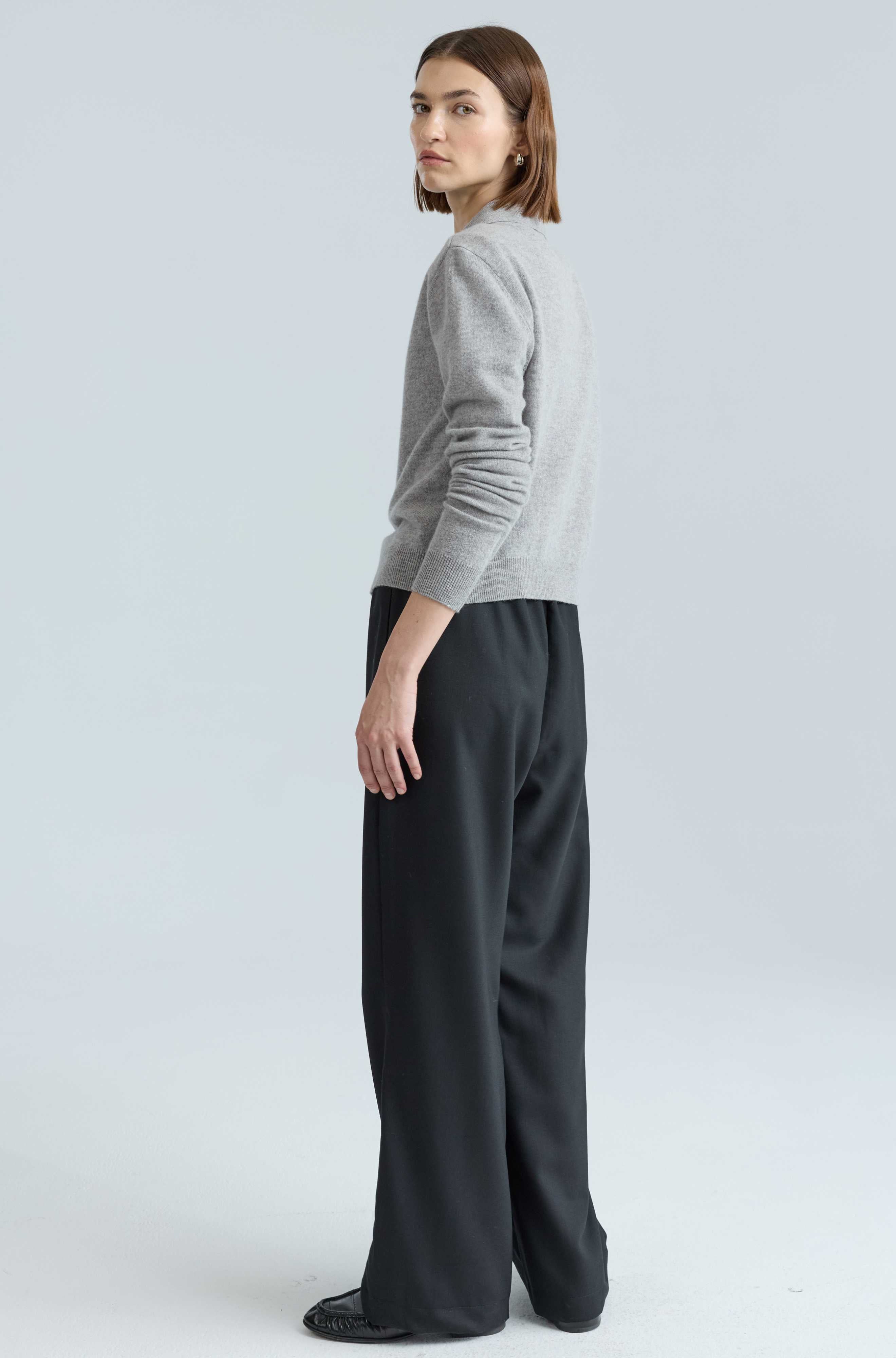 Person wearing a gray sweater and black pants on a light gray background