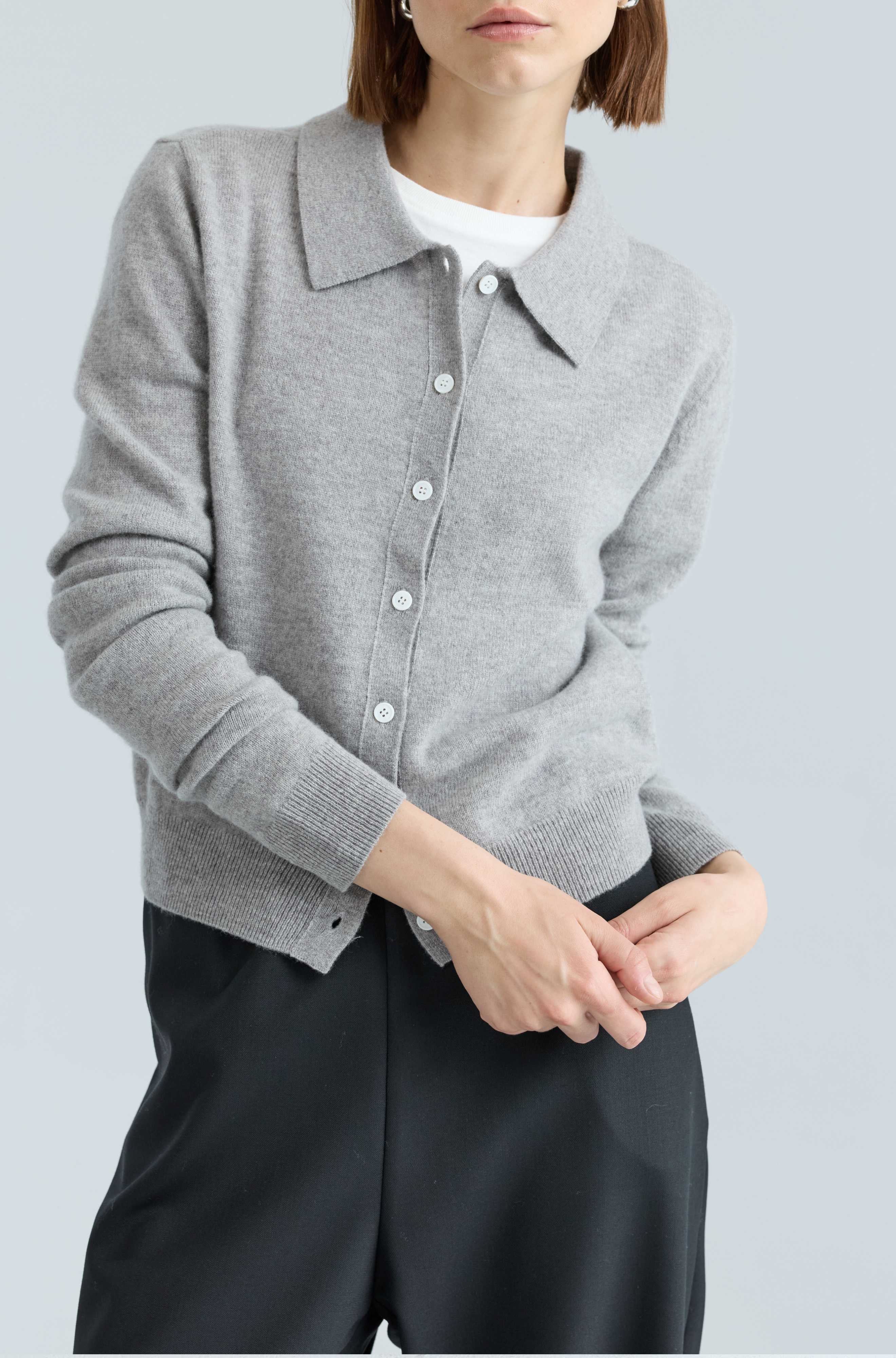 Person wearing a gray cardigan over a white shirt with black pants on a light gray background