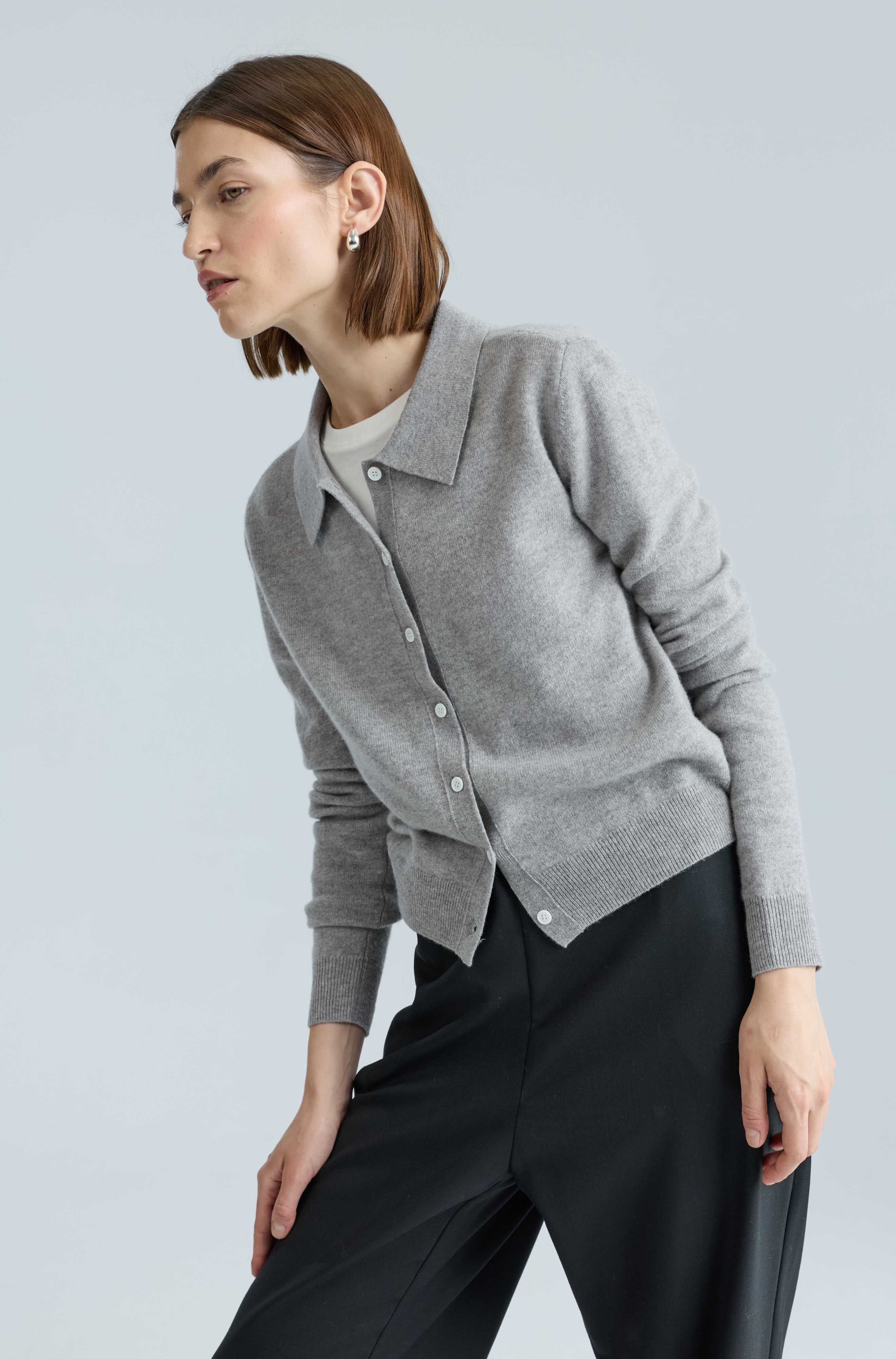 Woman wearing a gray cardigan over a white shirt on a light gray background