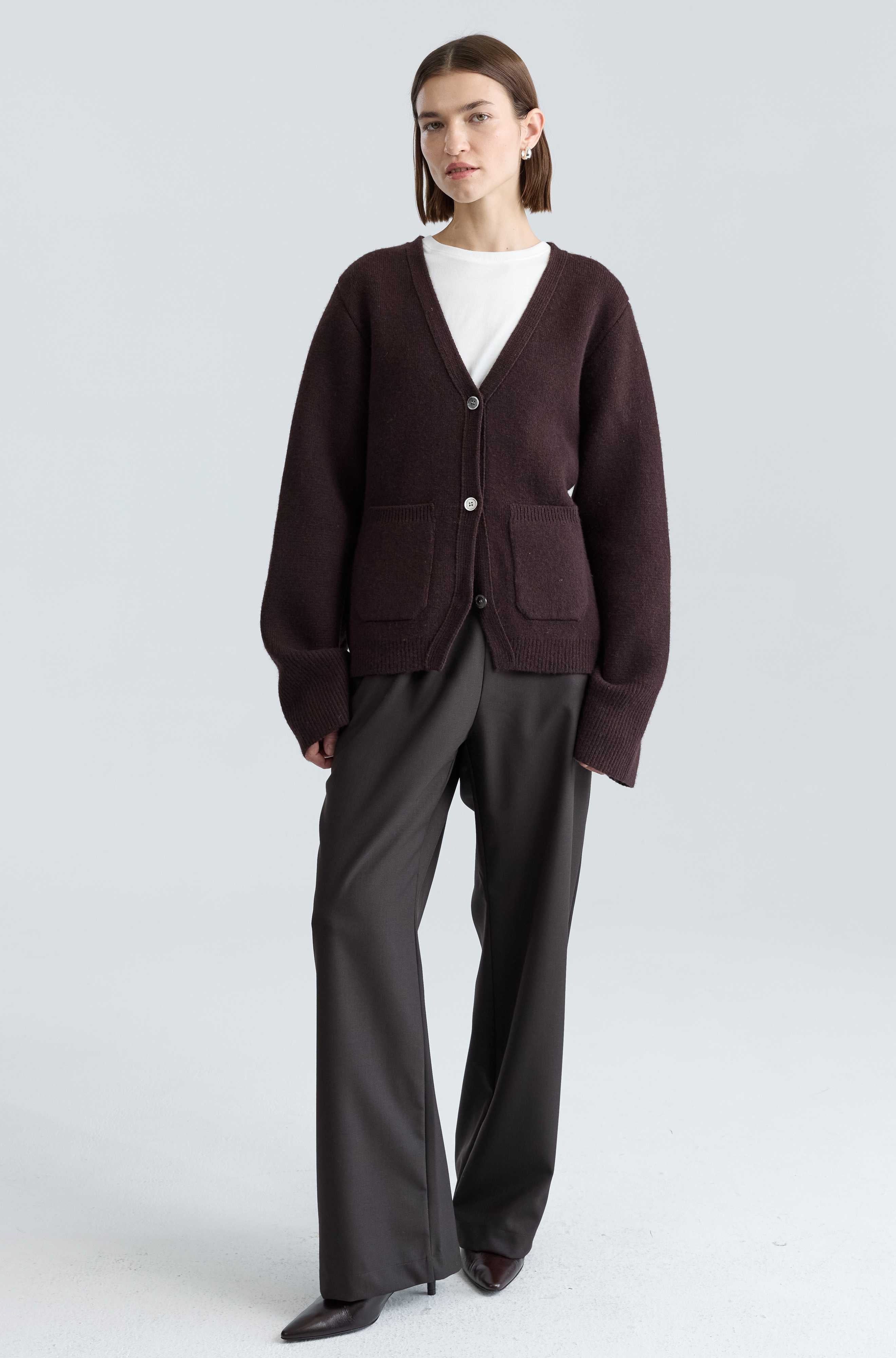 Person wearing a brown cardigan and gray pants on a white background