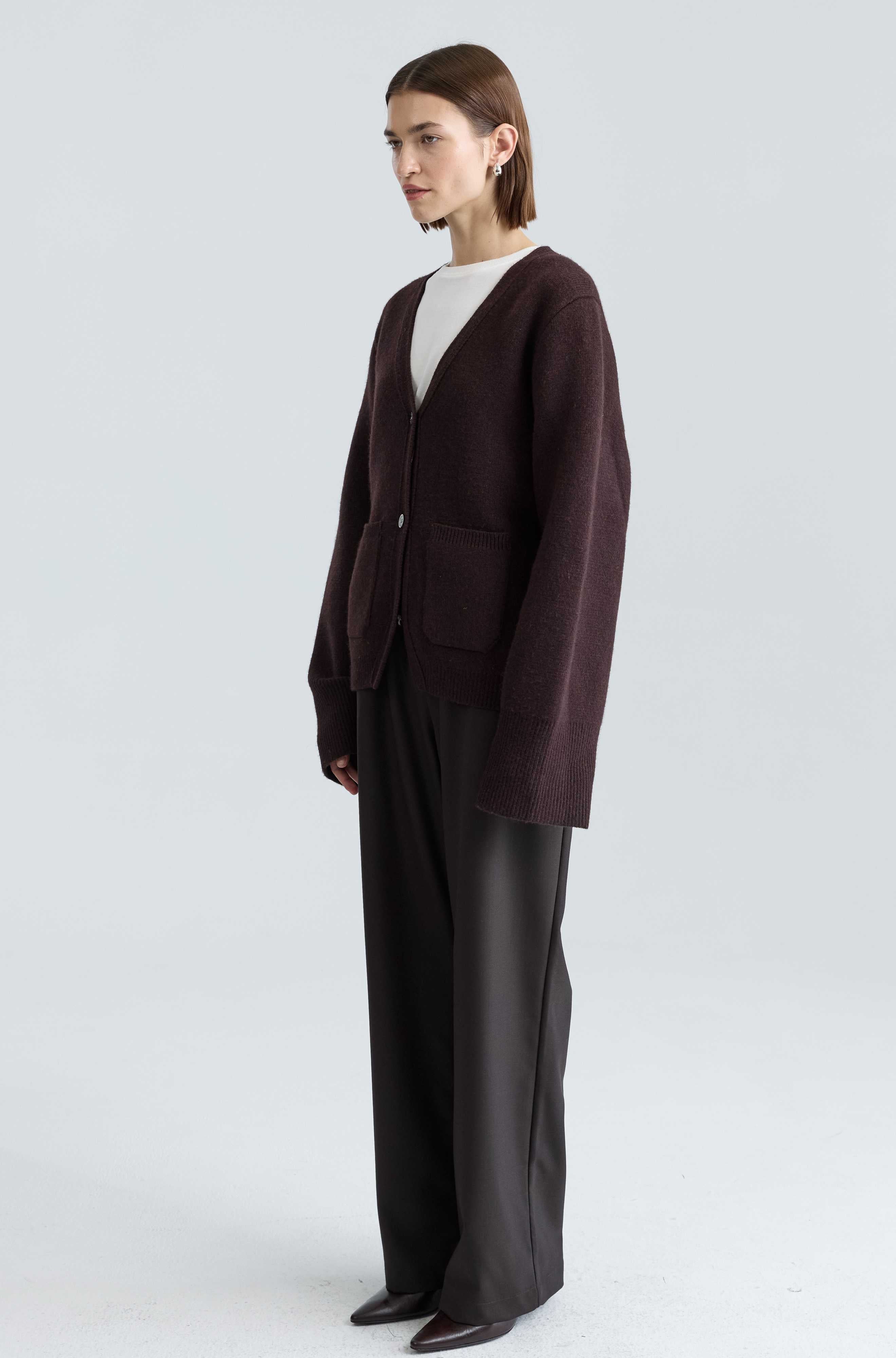 Person wearing a brown cardigan and black pants on a white background