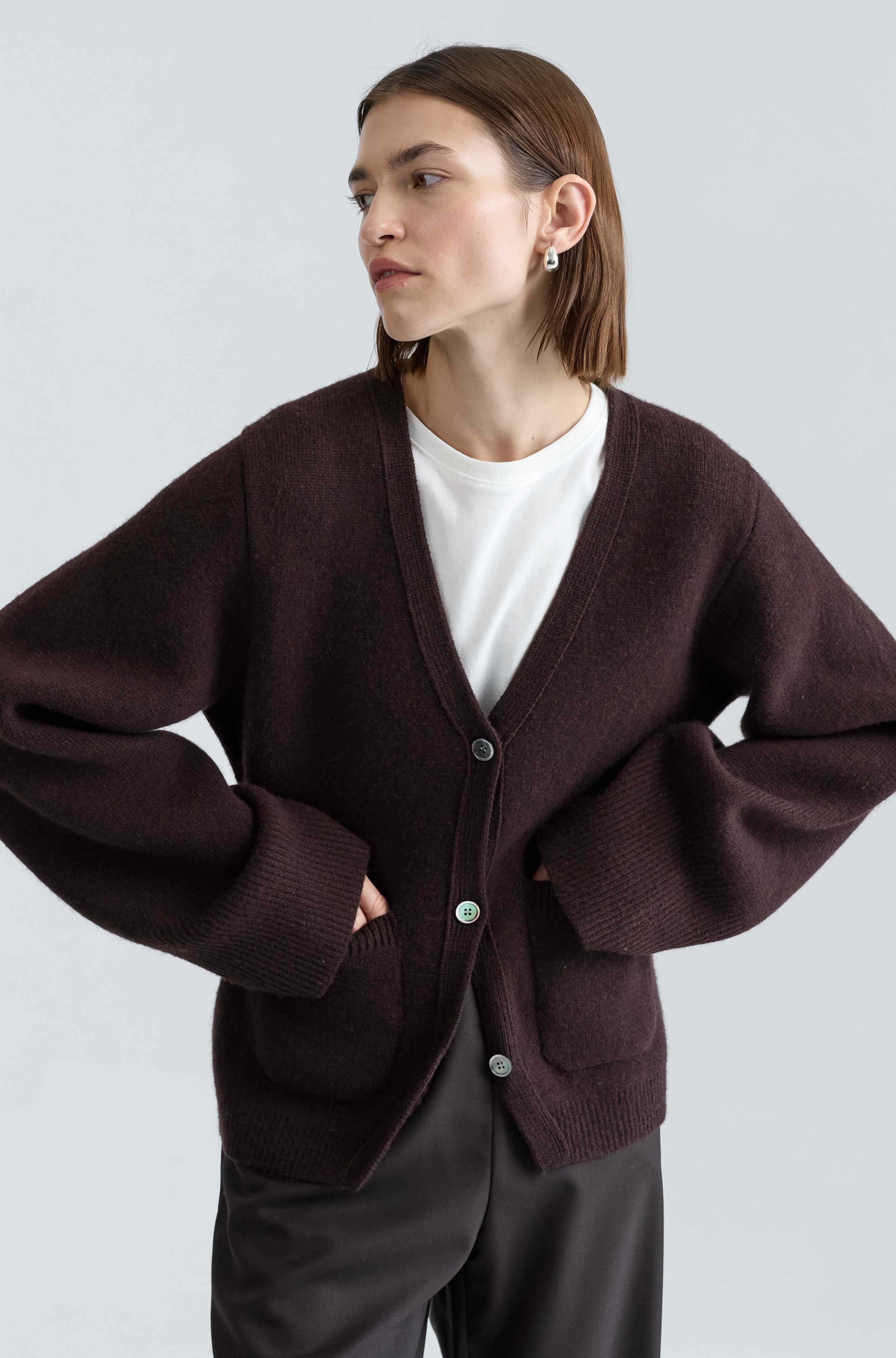 Woman wearing a brown cardigan over a white shirt on a light gray background